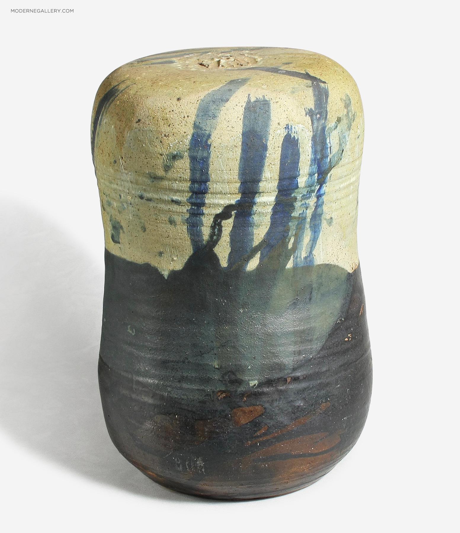 Ceramic vase with abstract blue and black glaze patterns on a beige and dark base, against a white background.