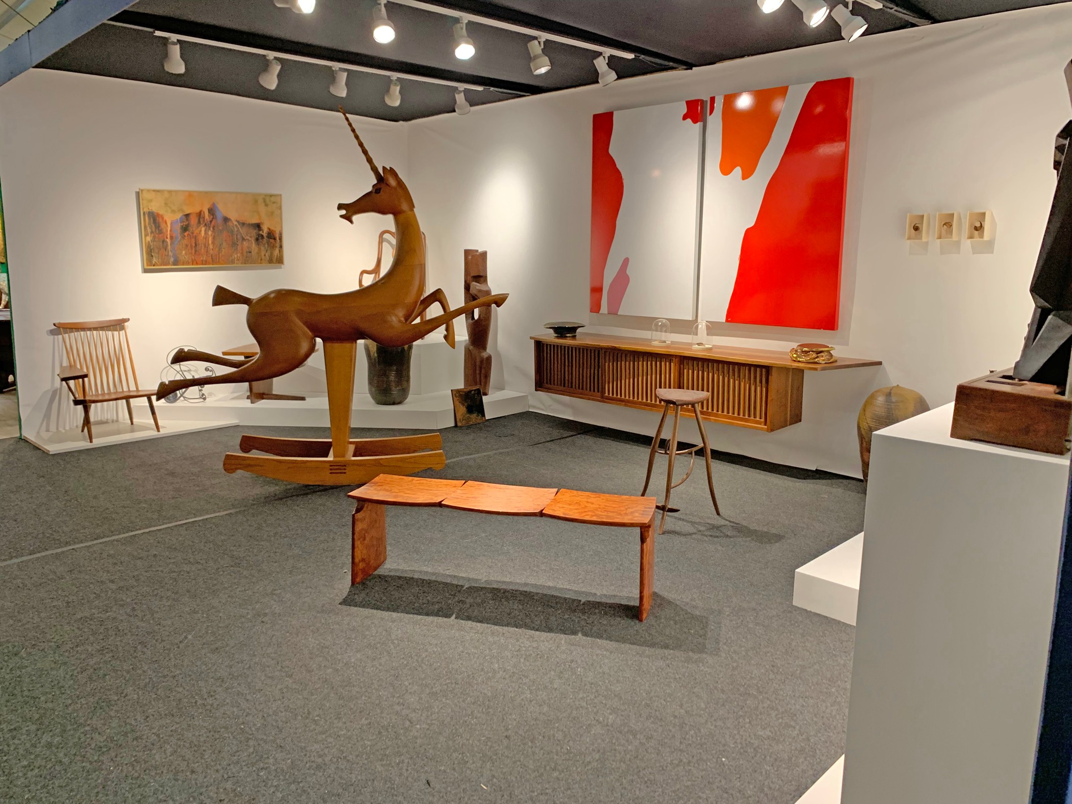 Gallery with a large deer sculpture, wooden bench, chairs, and abstract paintings on white walls.