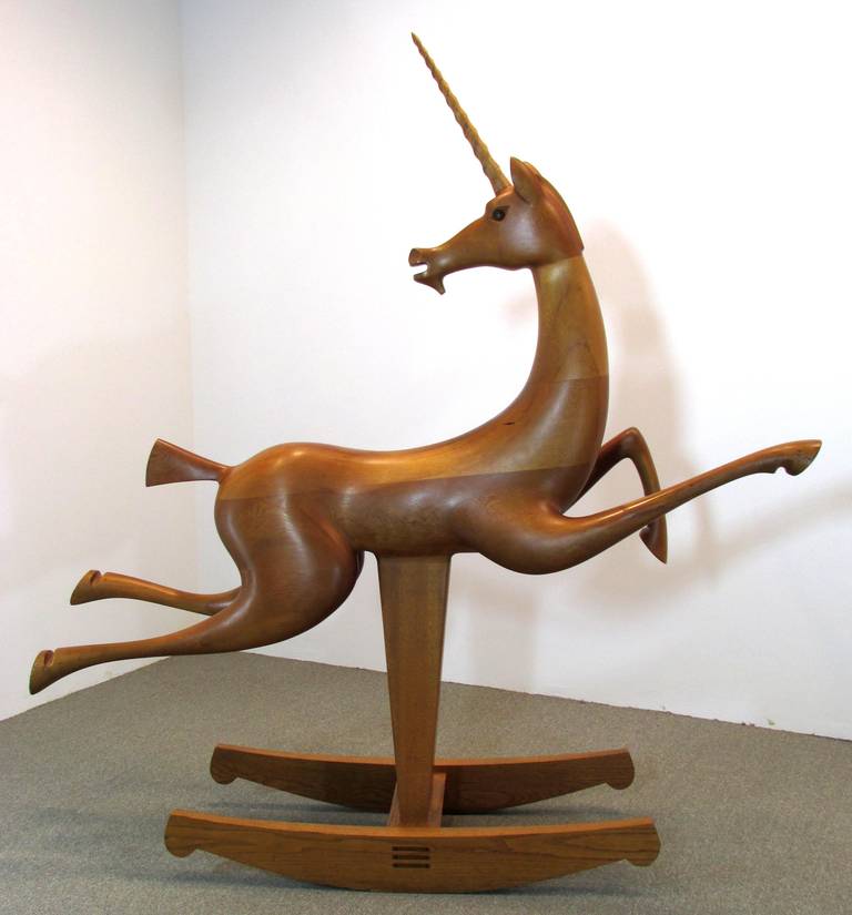 Wooden unicorn rocking horse with a horn, standing on a base, against a plain white wall.
