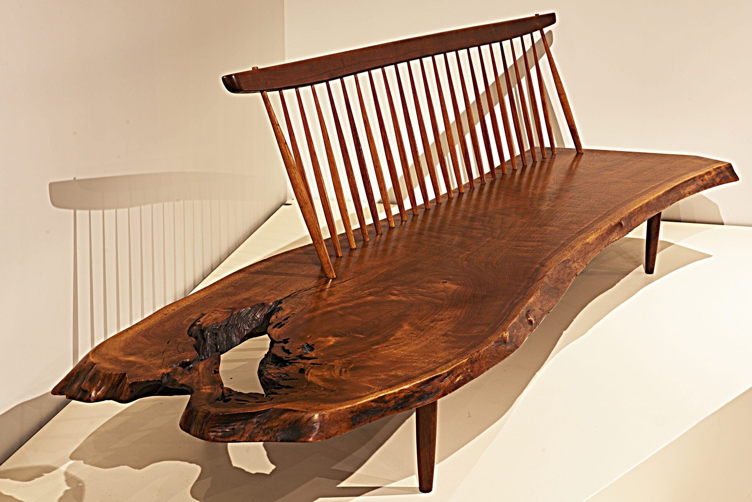 Wooden bench with a curved seat and a slatted backrest, supported by four legs, on a white surface.