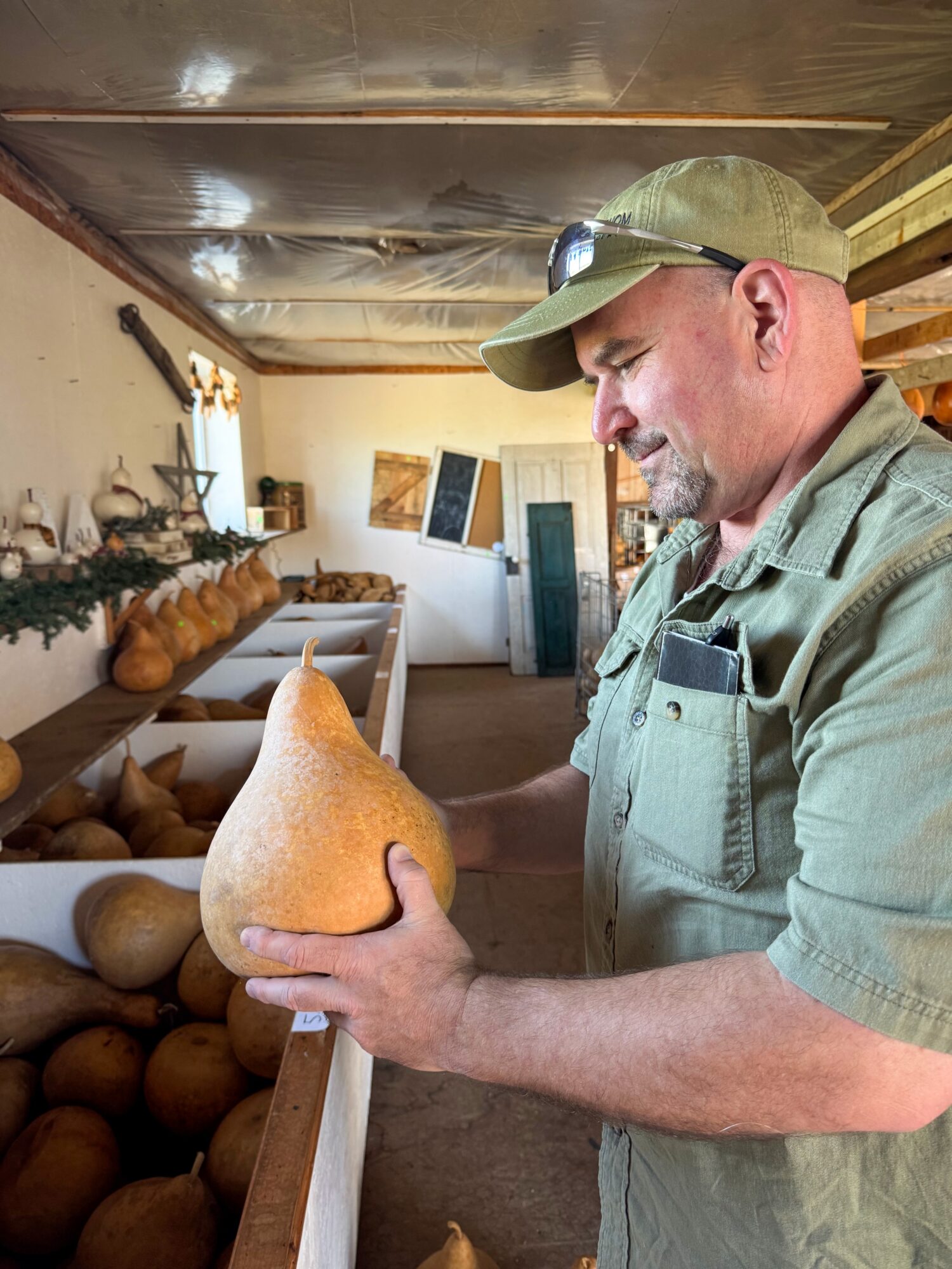 Man in uniform holding a large pear-shaped object in a room with wooden shelves and baked goods.