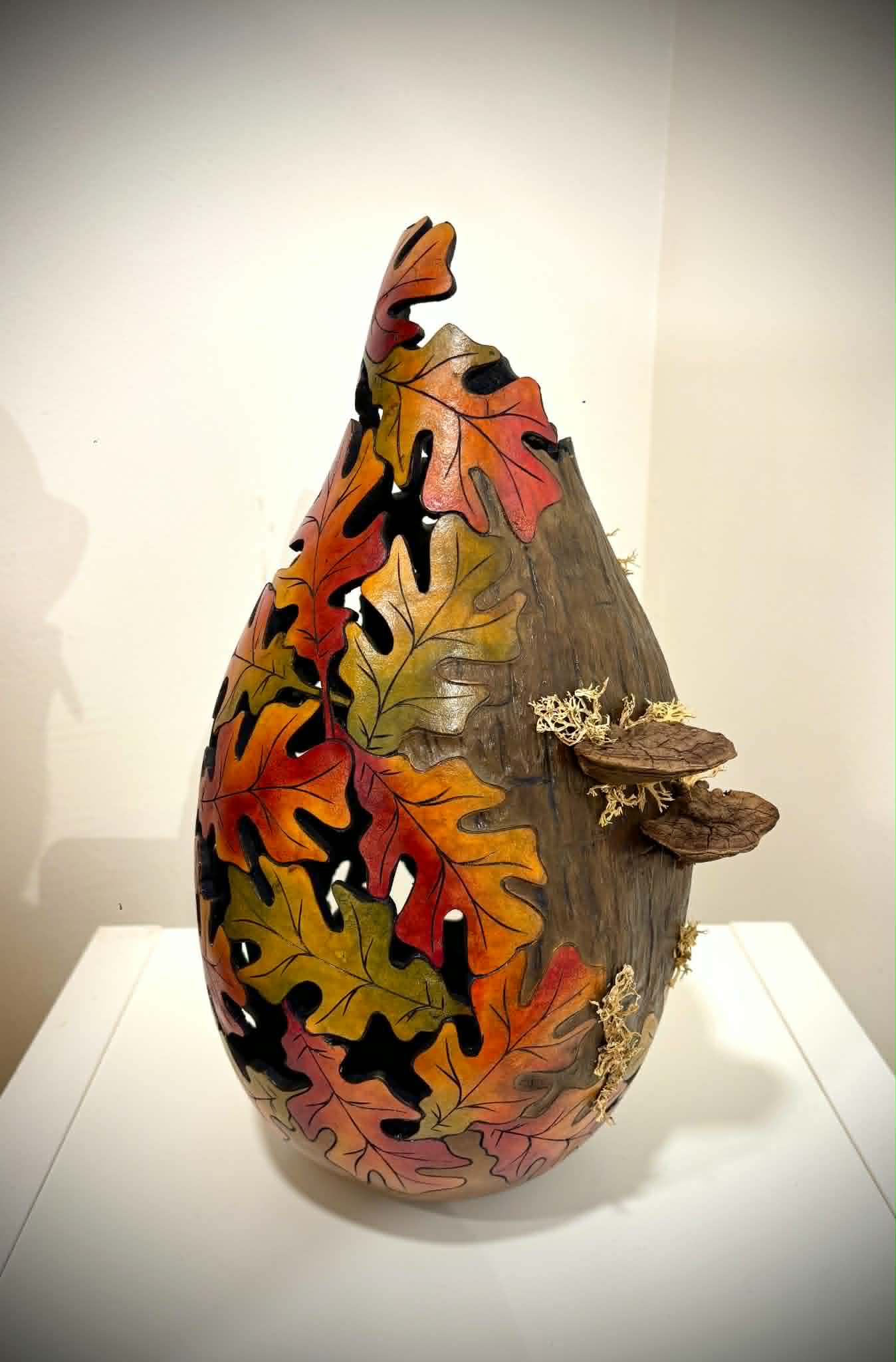 Decorative ceramic vase with painted autumn leaves and a small branch protruding from the side.