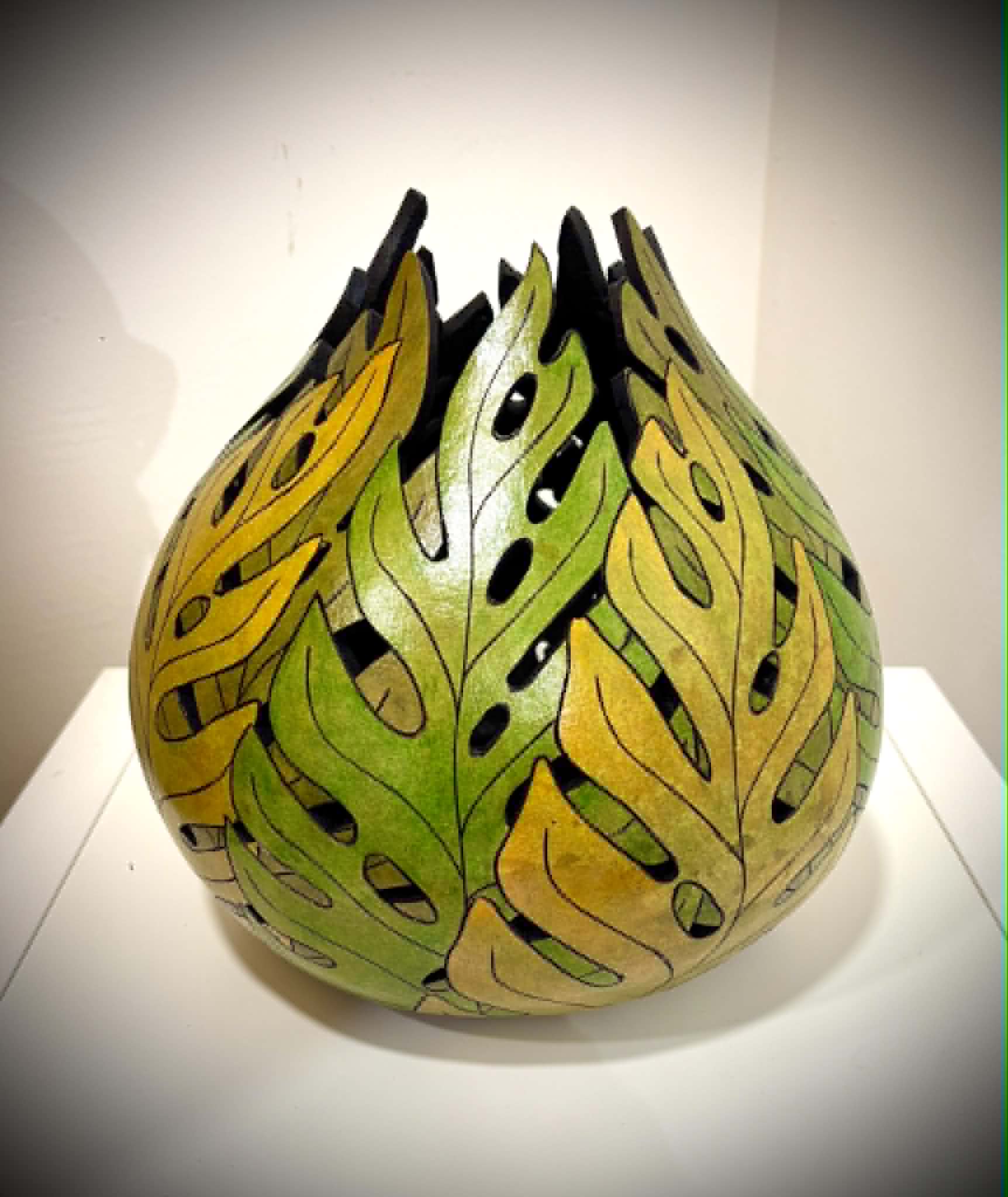 Colorful ceramic vase with leaf patterns in yellow, green, and black, displayed on a white surface against a plain background.