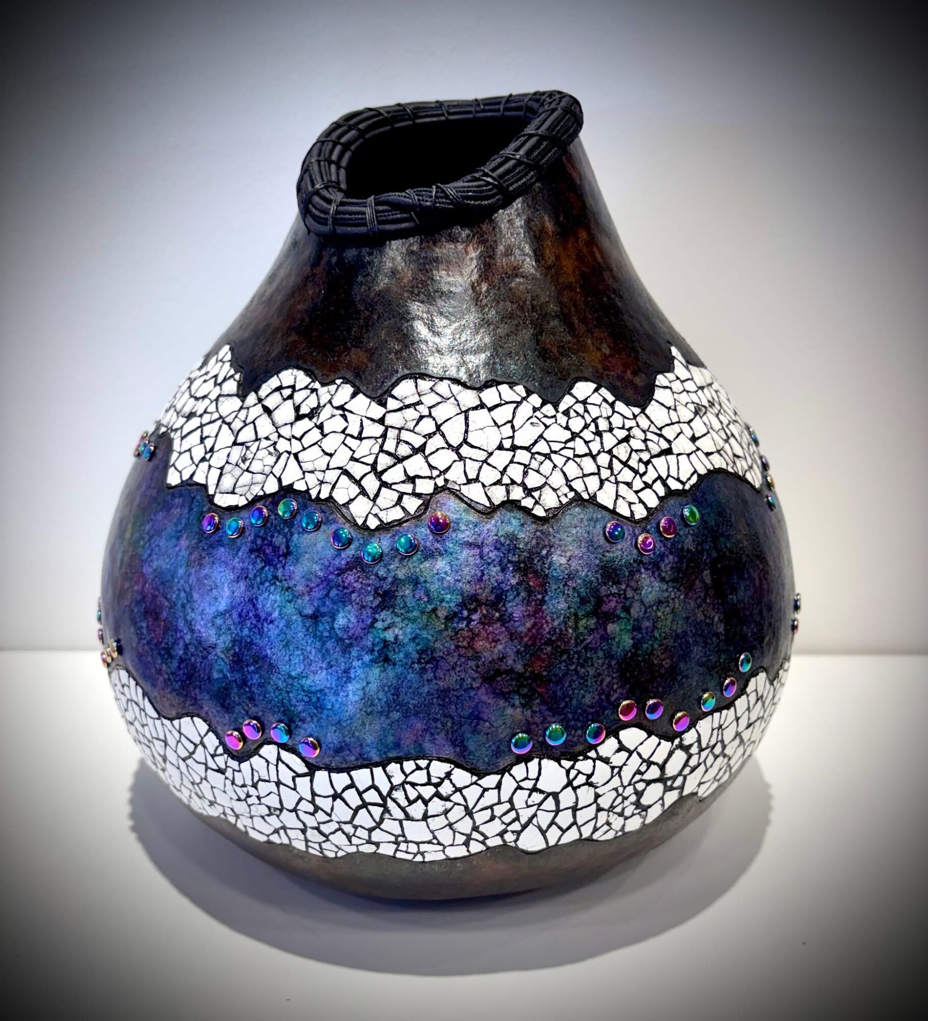 Decorative vase with a black top, white cracked pattern, and a central blue and purple iridescent band, on a white surface.