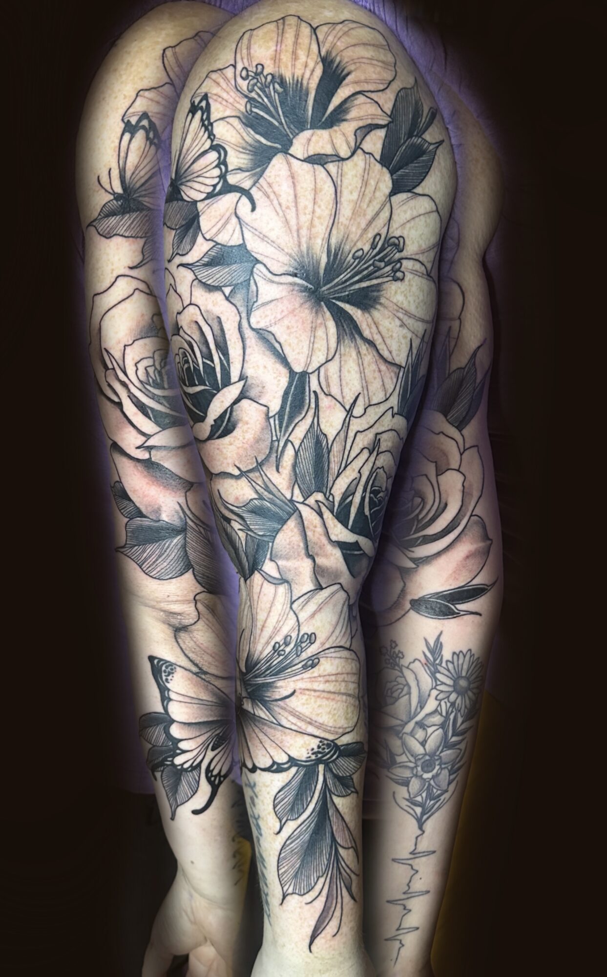 Tattoo of large flowers and leaves covering shoulder and arm, with detailed line work and shading.