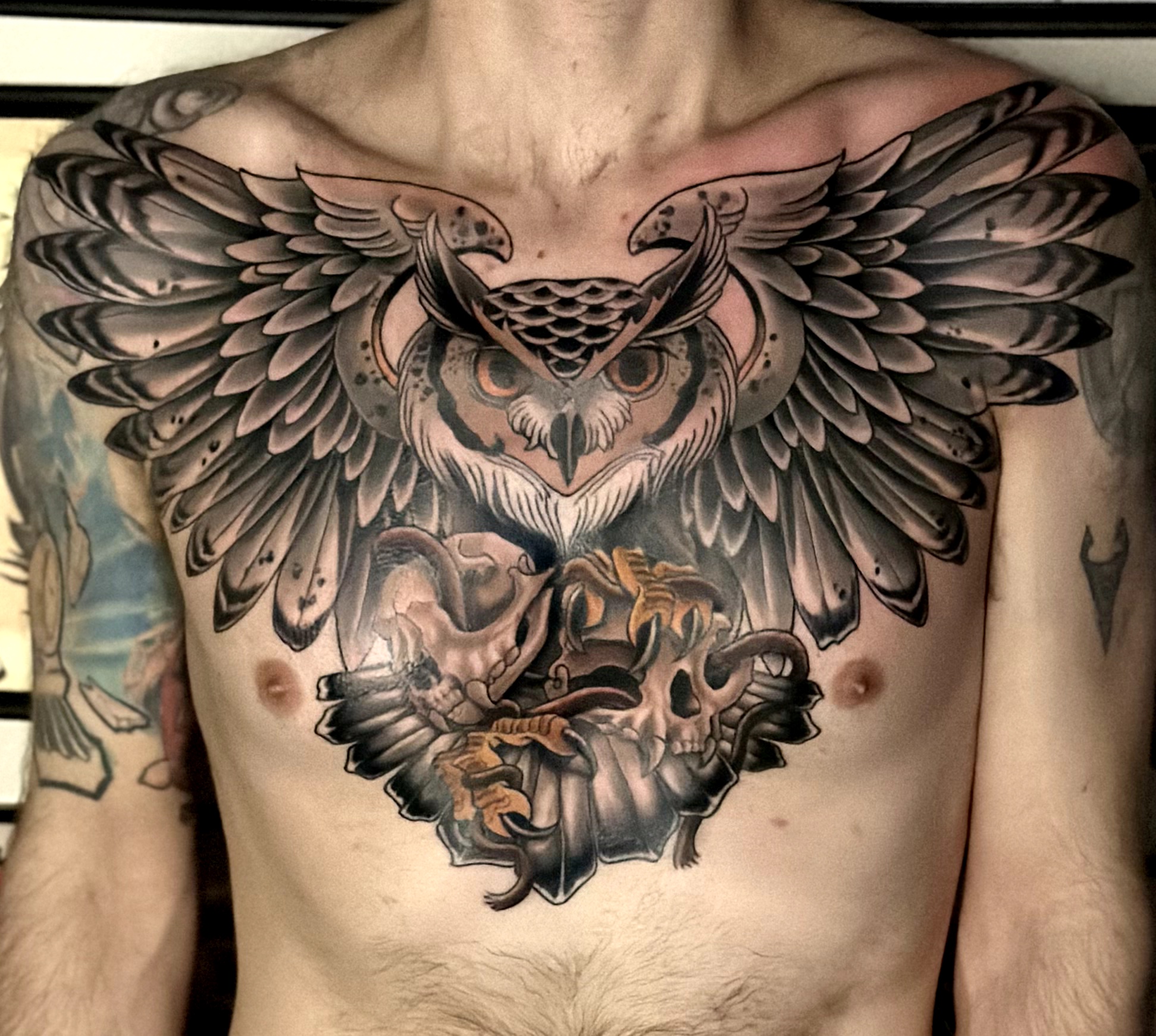 Large owl tattoo with spread wings covers chest, detailed feathers, and a fierce expression, with a lion and skull below. Word count: 20
