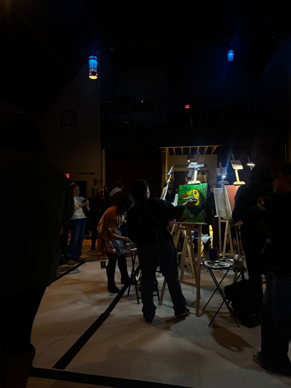 People gathered around an art installation or exhibit in a dimly lit indoor space with spotlights, some working on or observing the display.