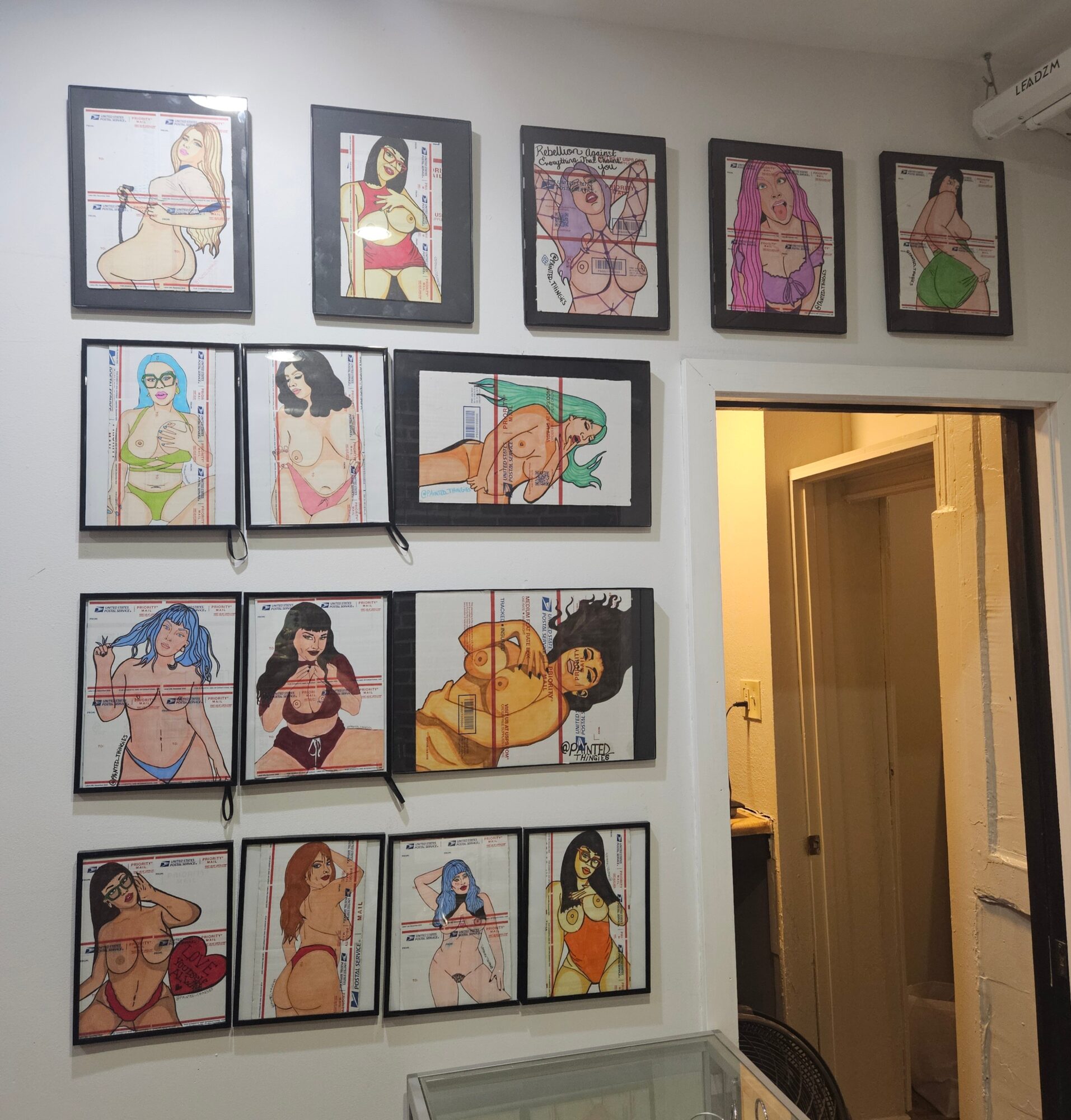 Wall with framed colorful illustrations of women in various poses, arranged in three rows, with a doorway on the right side.