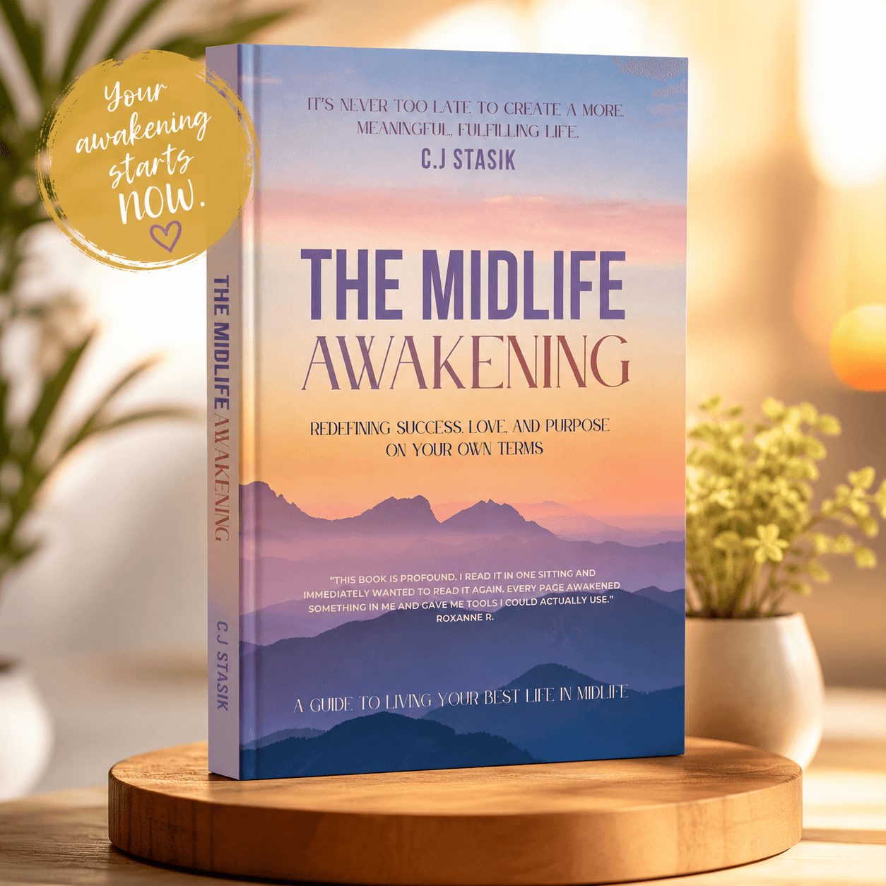 Book titled 'The Midlife Awakening' standing on a round wooden surface with a blurred background of a plant and light. A gold sticker says 'Your awakening starts now.'