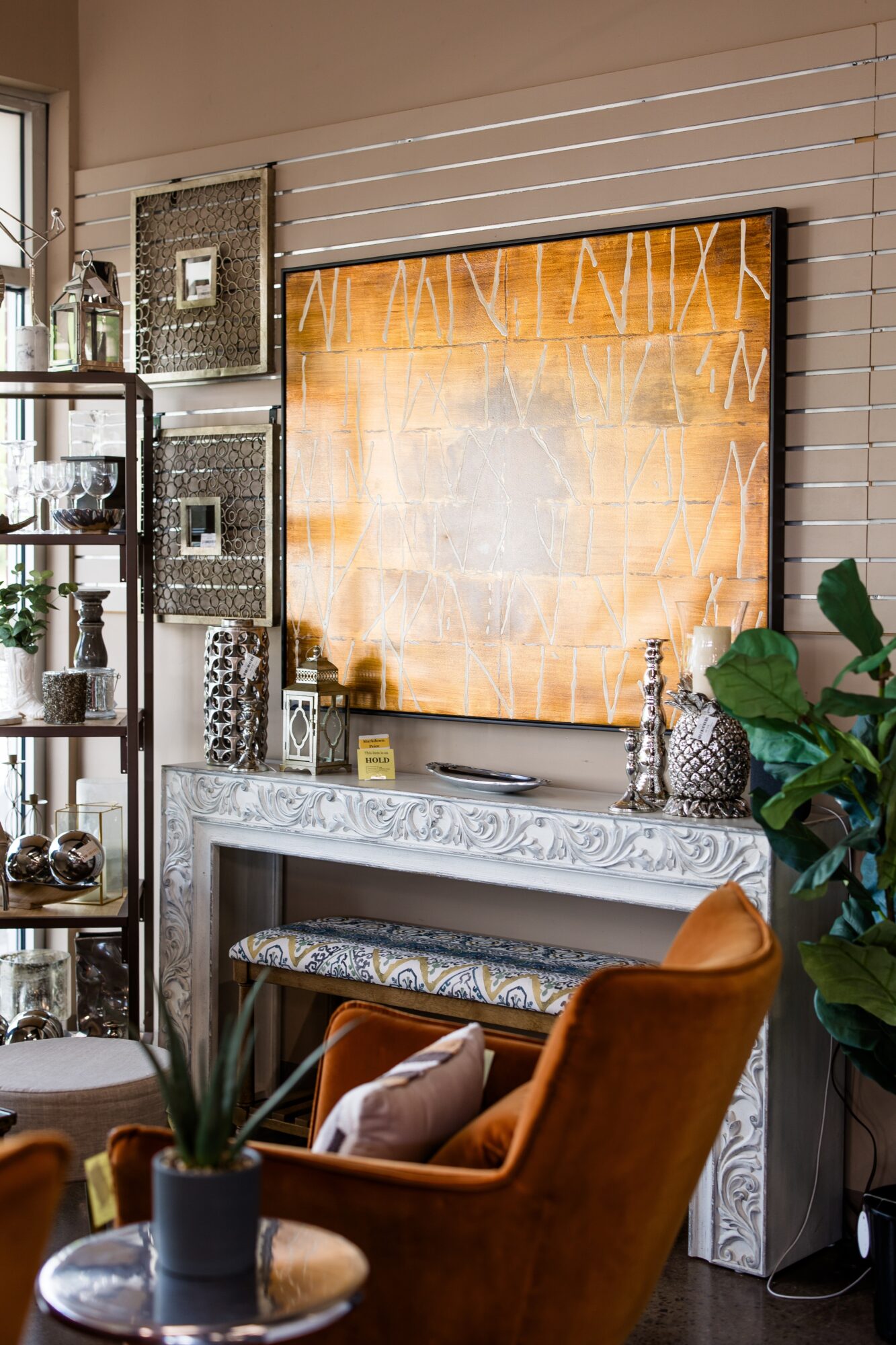 Living room with a large abstract orange and white painting, fireplace mantel, armchair, and plants.
