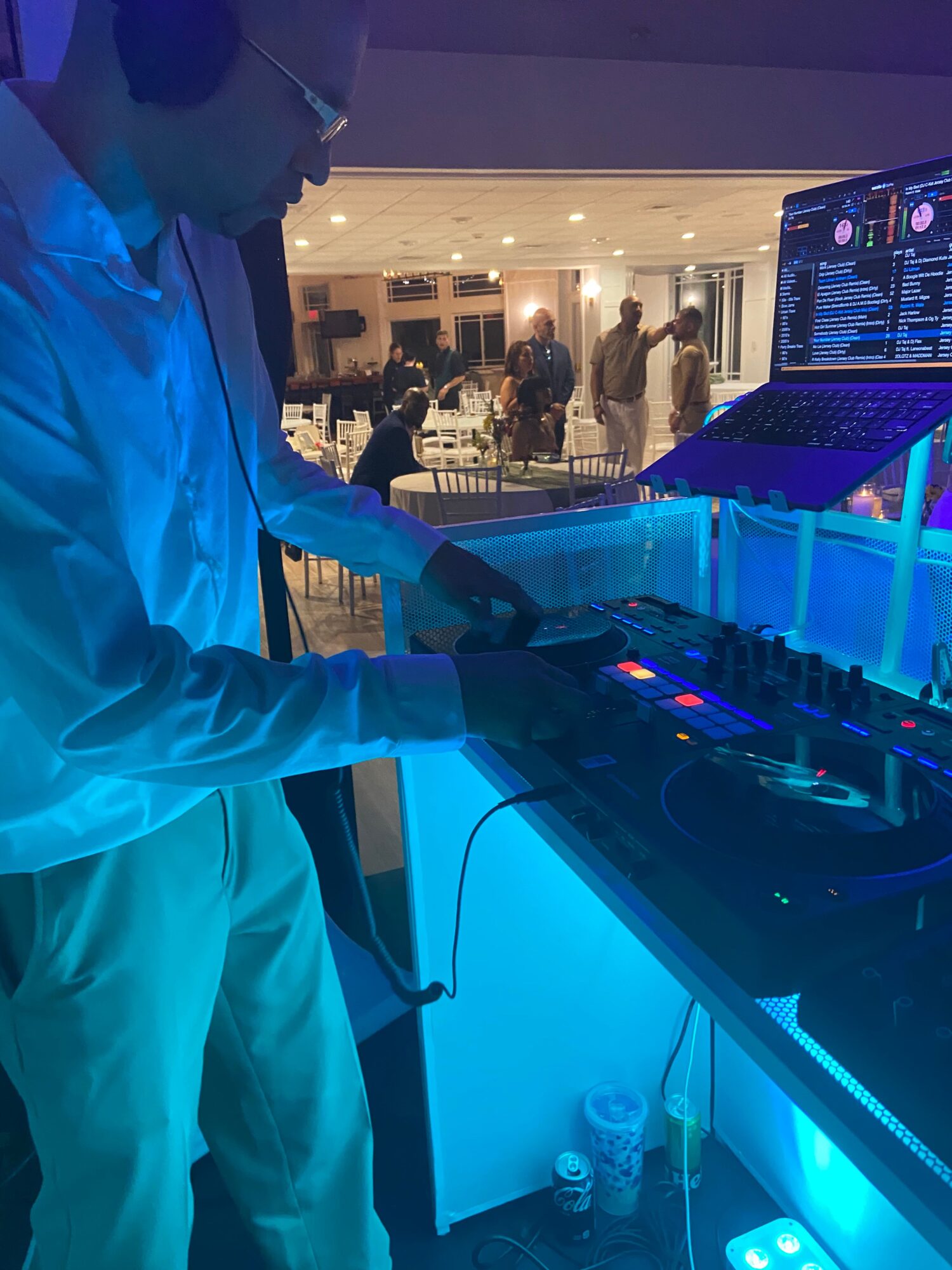 Person in a white coat operating DJ equipment with blue lighting, in a modern indoor space.