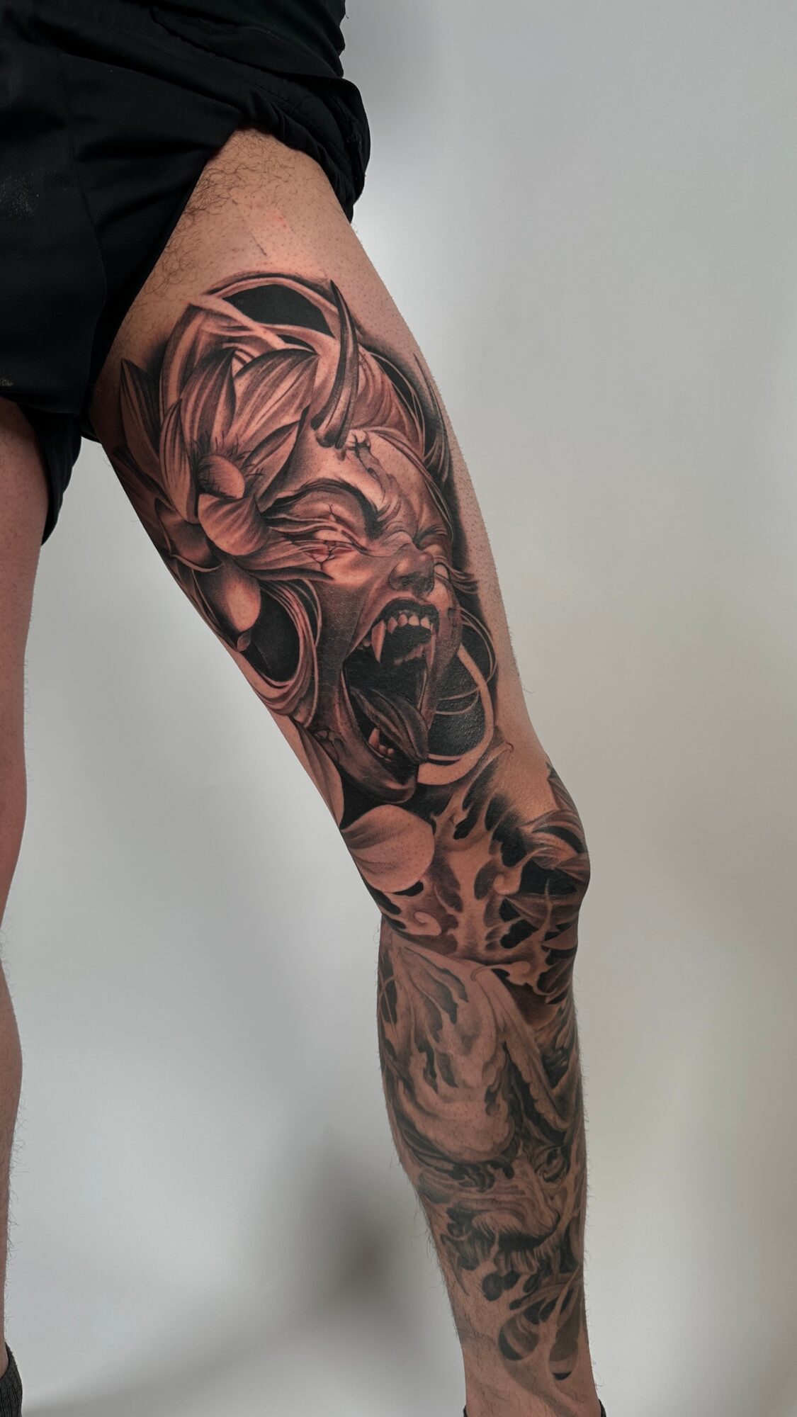 Tattooed leg featuring a roaring lion's face and floral elements, detailed in black and gray ink.
