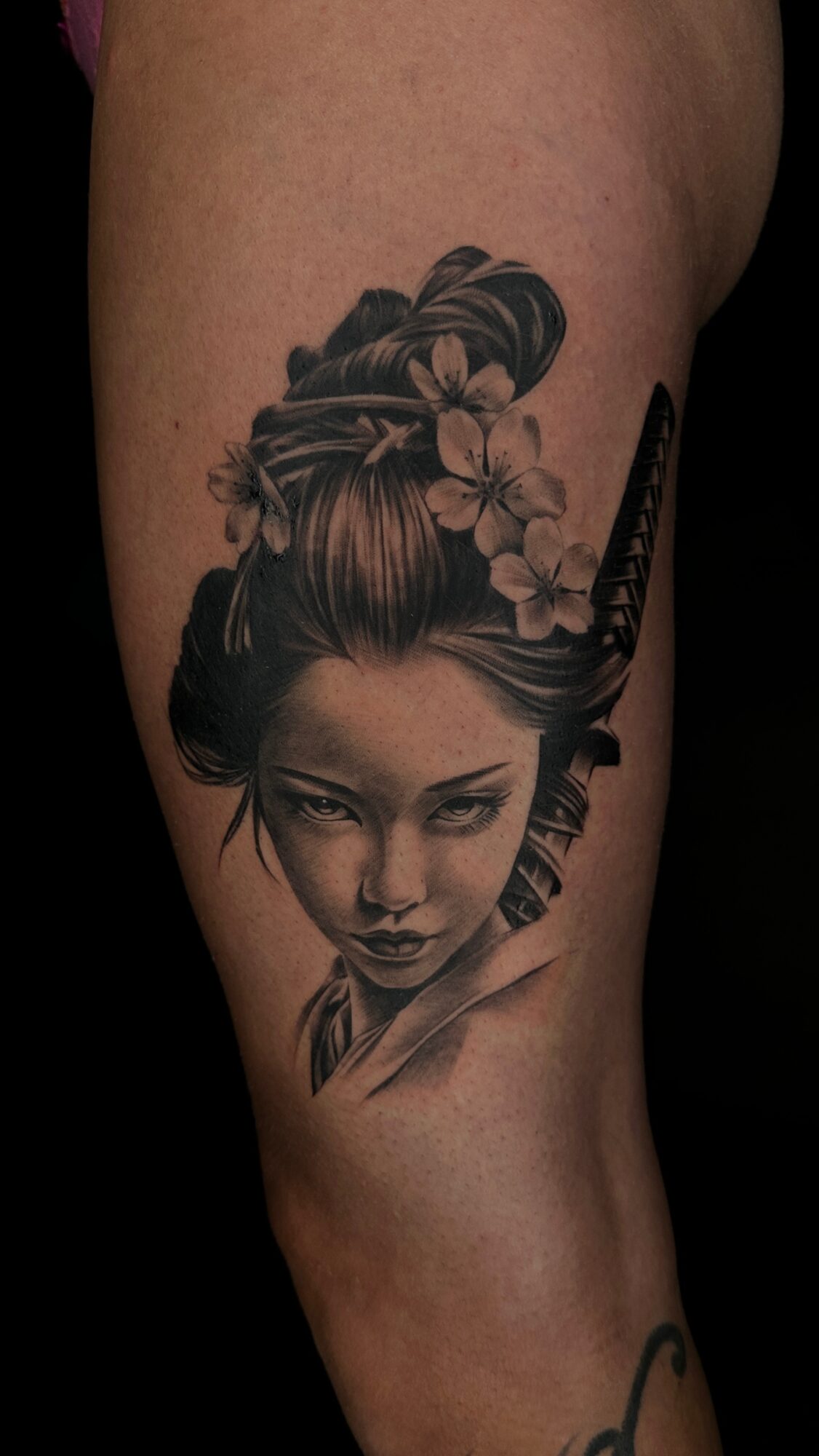 Black and gray tattoo of a woman with traditional Japanese hairstyle and hair accessories, holding a katana sword.