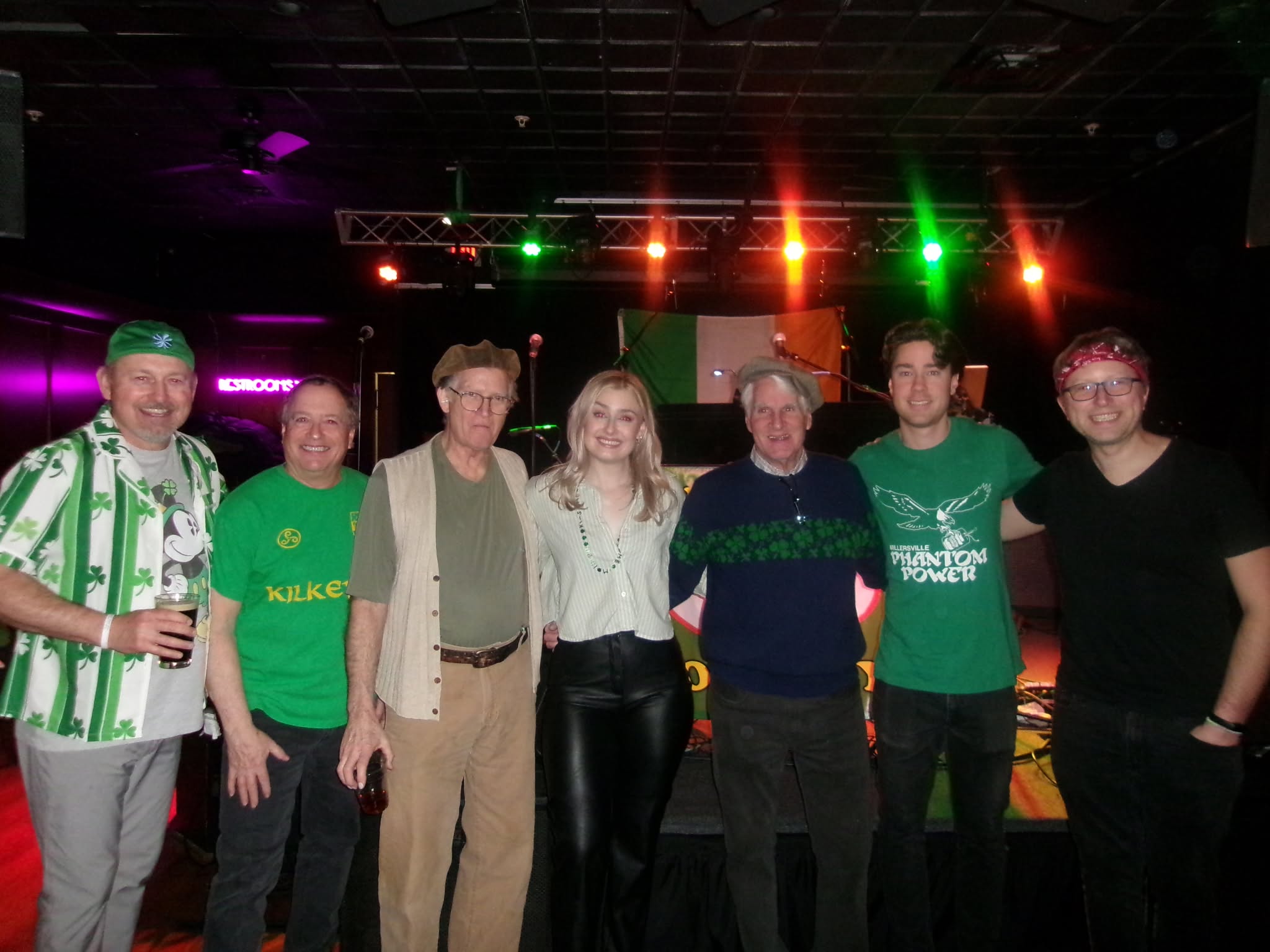 Group of seven people standing together on a stage with colorful lights overhead, smiling at the camera.
