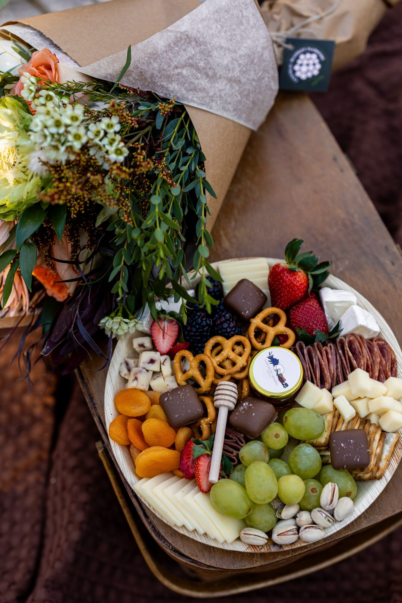 A bouquet of flowers and a box of assorted chocolates and fruits on a table.