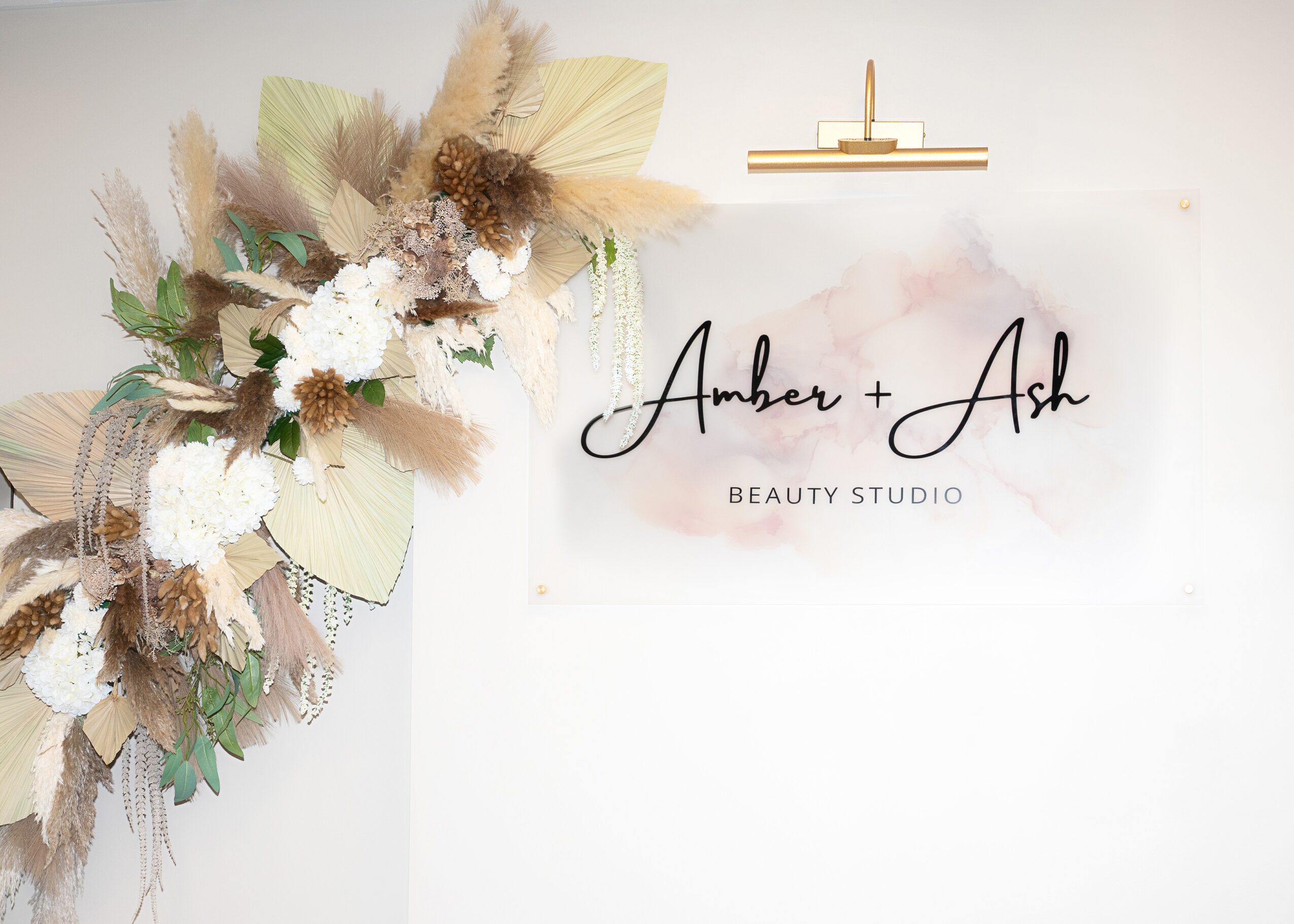 Decorative floral arrangement with dried flowers and leaves next to a sign reading 'Amber + Ash Beauty Studio'.