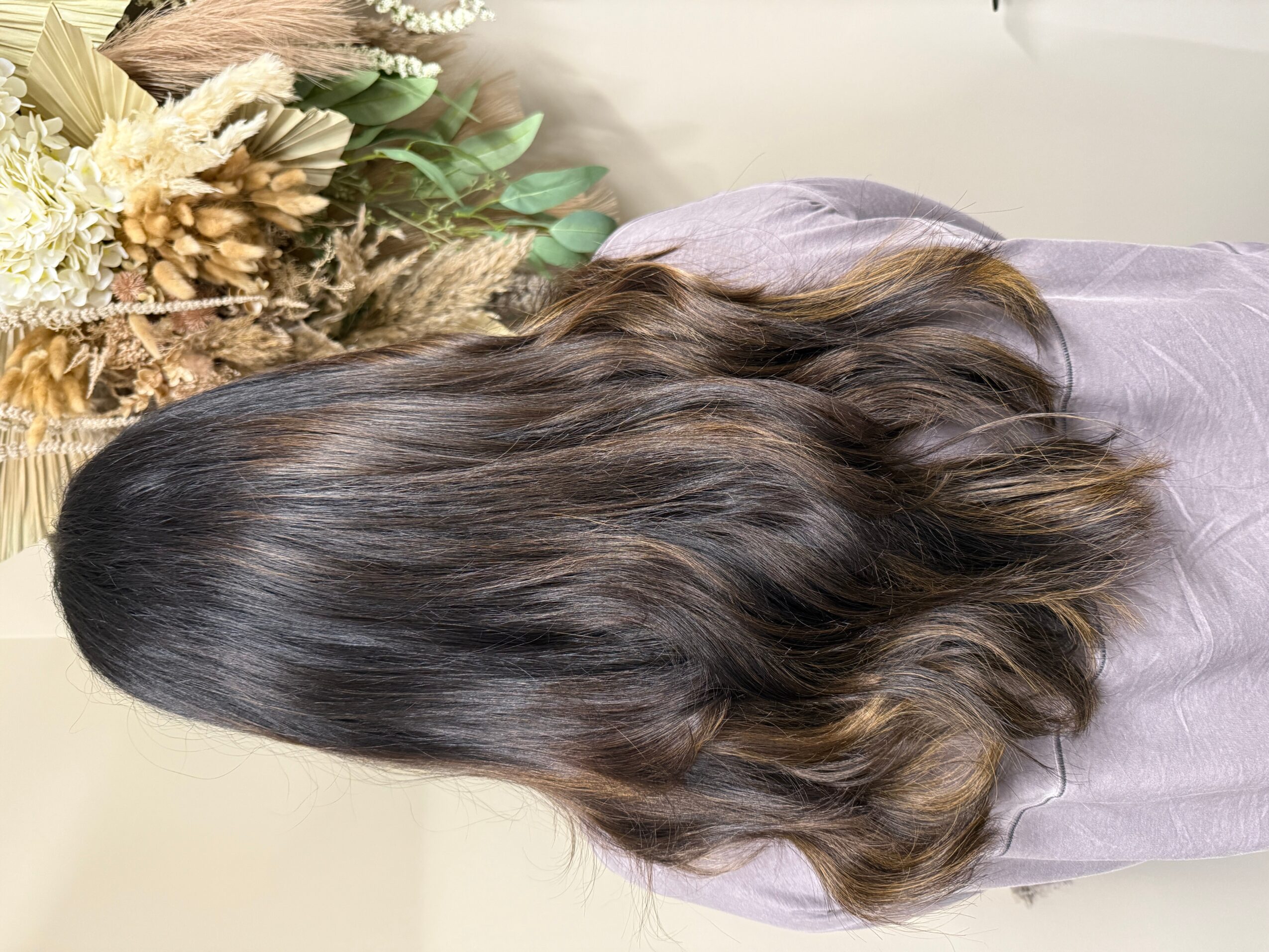 Person with long, wavy dark hair, seen from behind, wearing a gray top, with a floral arrangement nearby.