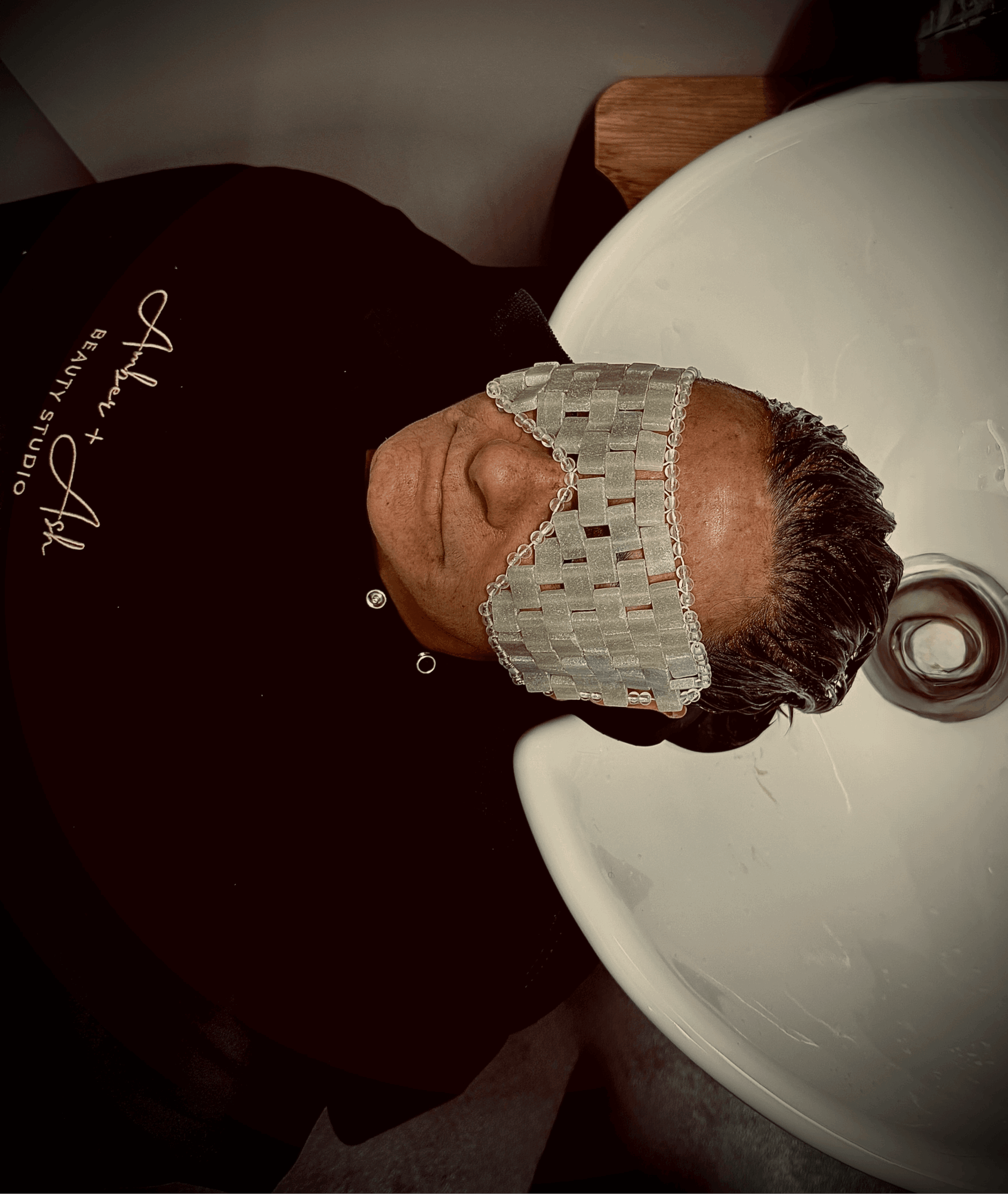 Person lying on a bed with a bandage over their eyes, head resting on a pillow, in a room with a white wall.