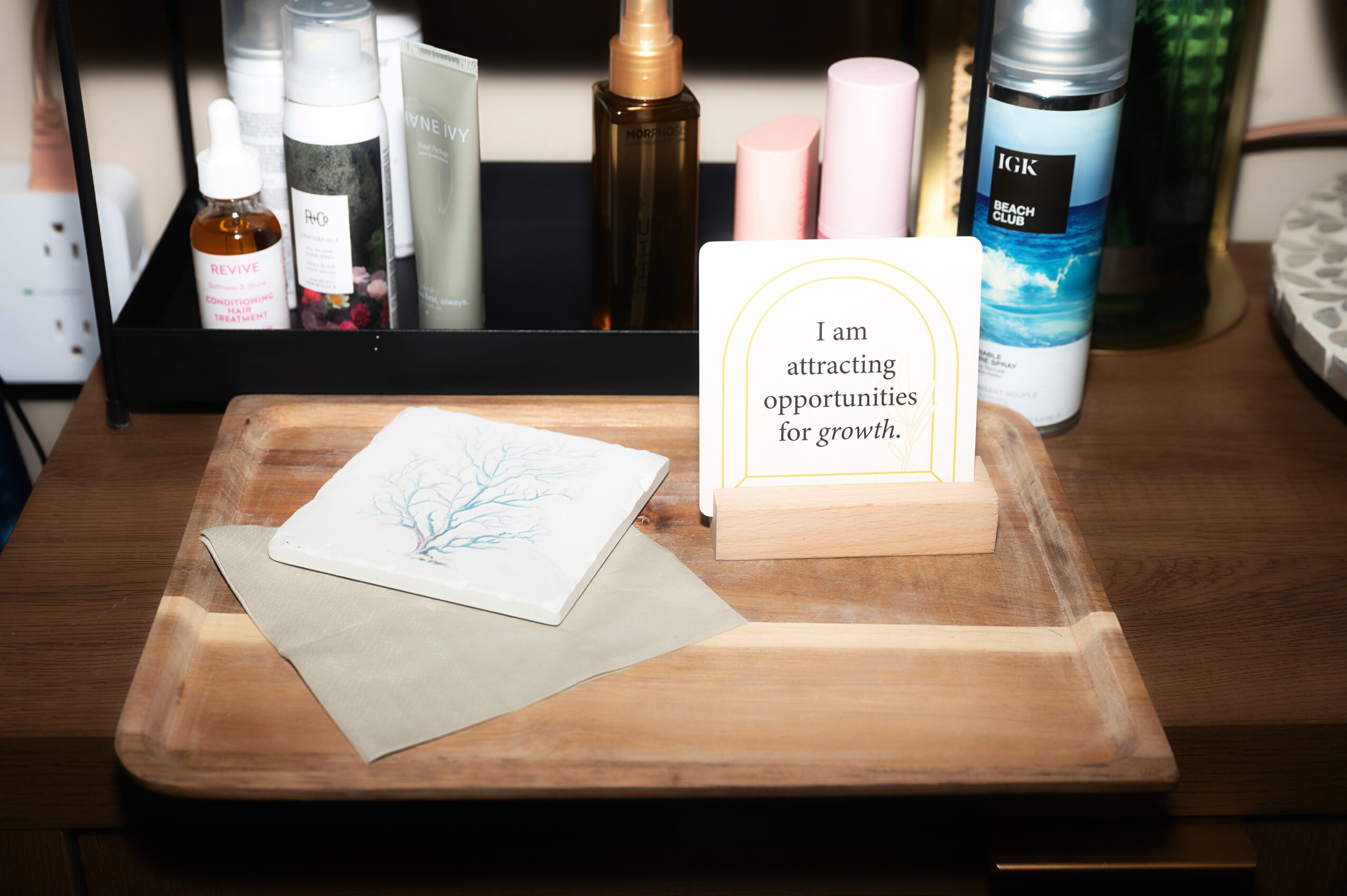 Wooden tray with a card and a small sign reading, 'I am attracting opportunities for growth,' on a desk with bottles in the background.
