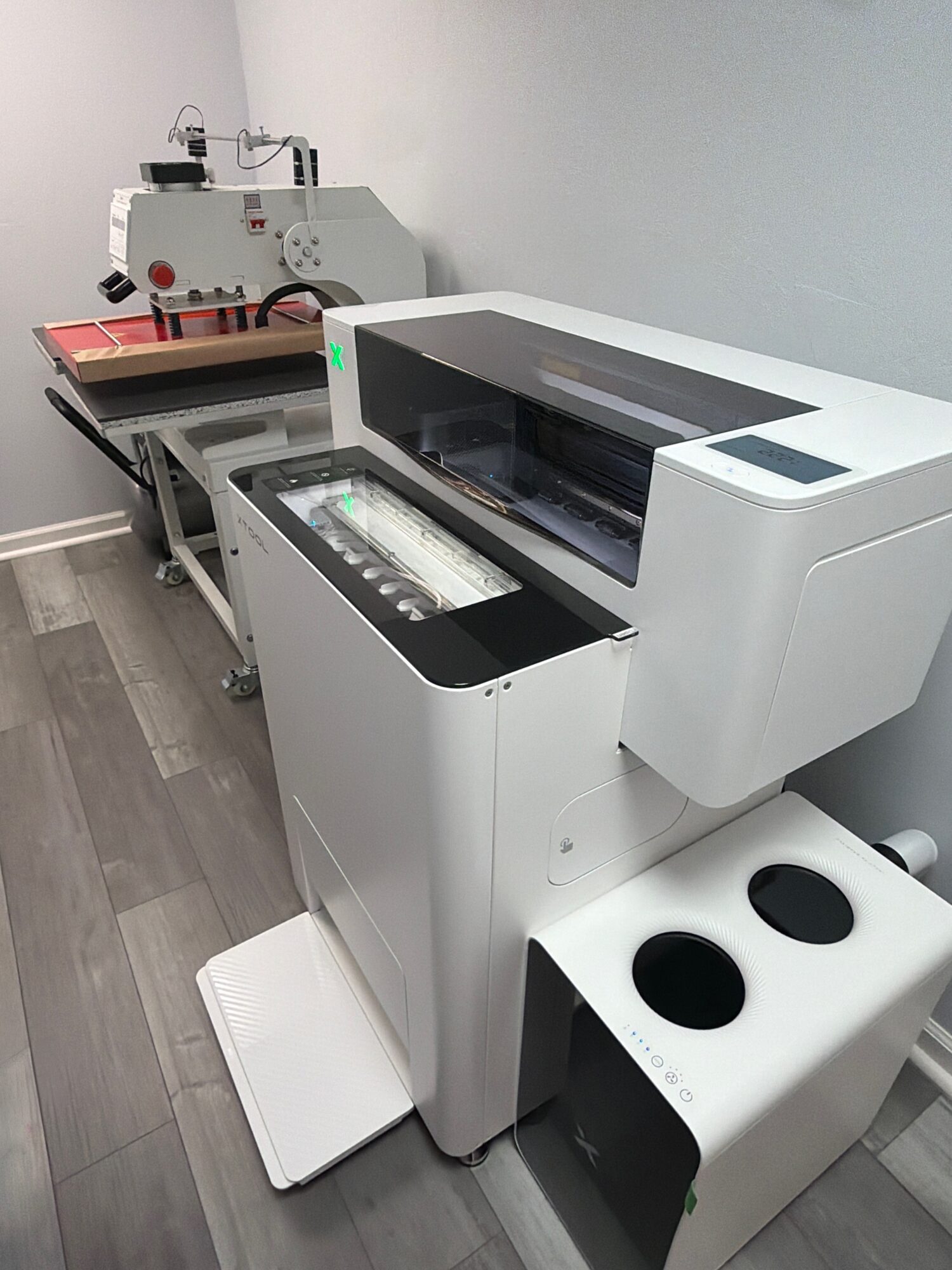 Laboratory with two large machines, one with a glass top and another with a transparent cover, on a gray floor and white wall.