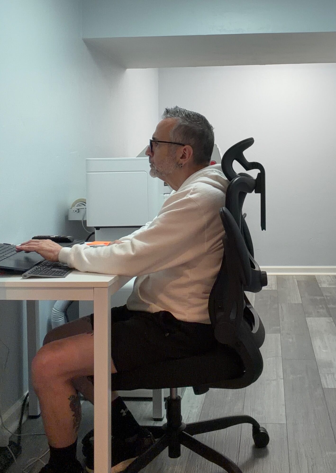 Man sitting at desk using computer in an office, with a chair backrest visible behind him.