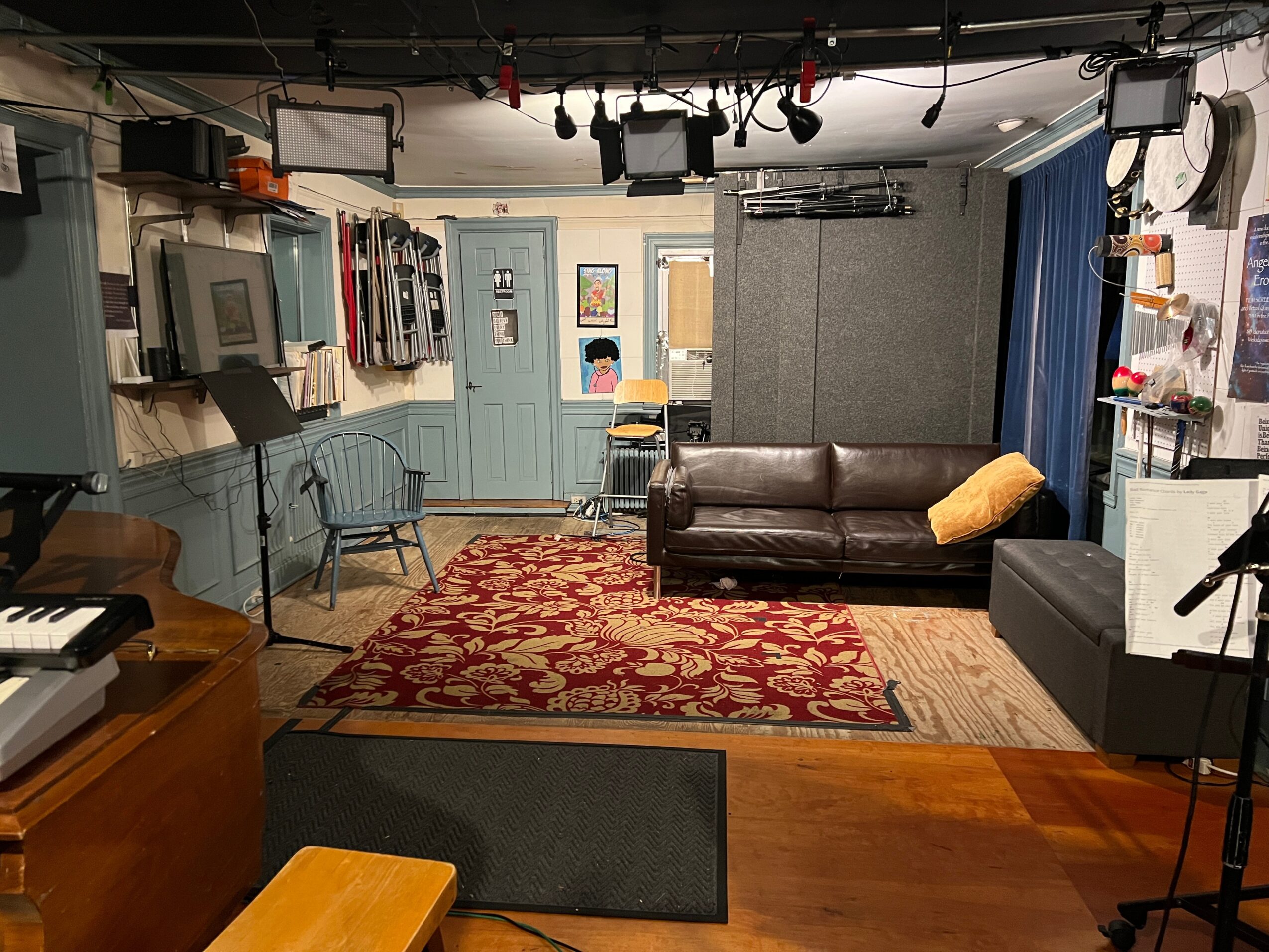Room with a brown sofa, blue curtains, patterned rug, and various equipment on walls, with a wooden floor and gray carpet.