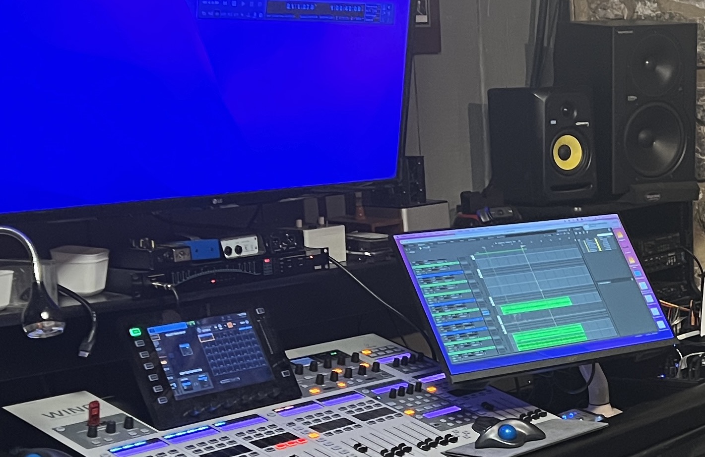 Music production setup with a large monitor, a tablet, and audio equipment on a desk.