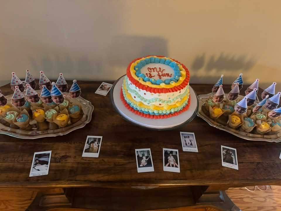 Birthday cake with colorful decorations, surrounded by party favors and photos on a table.