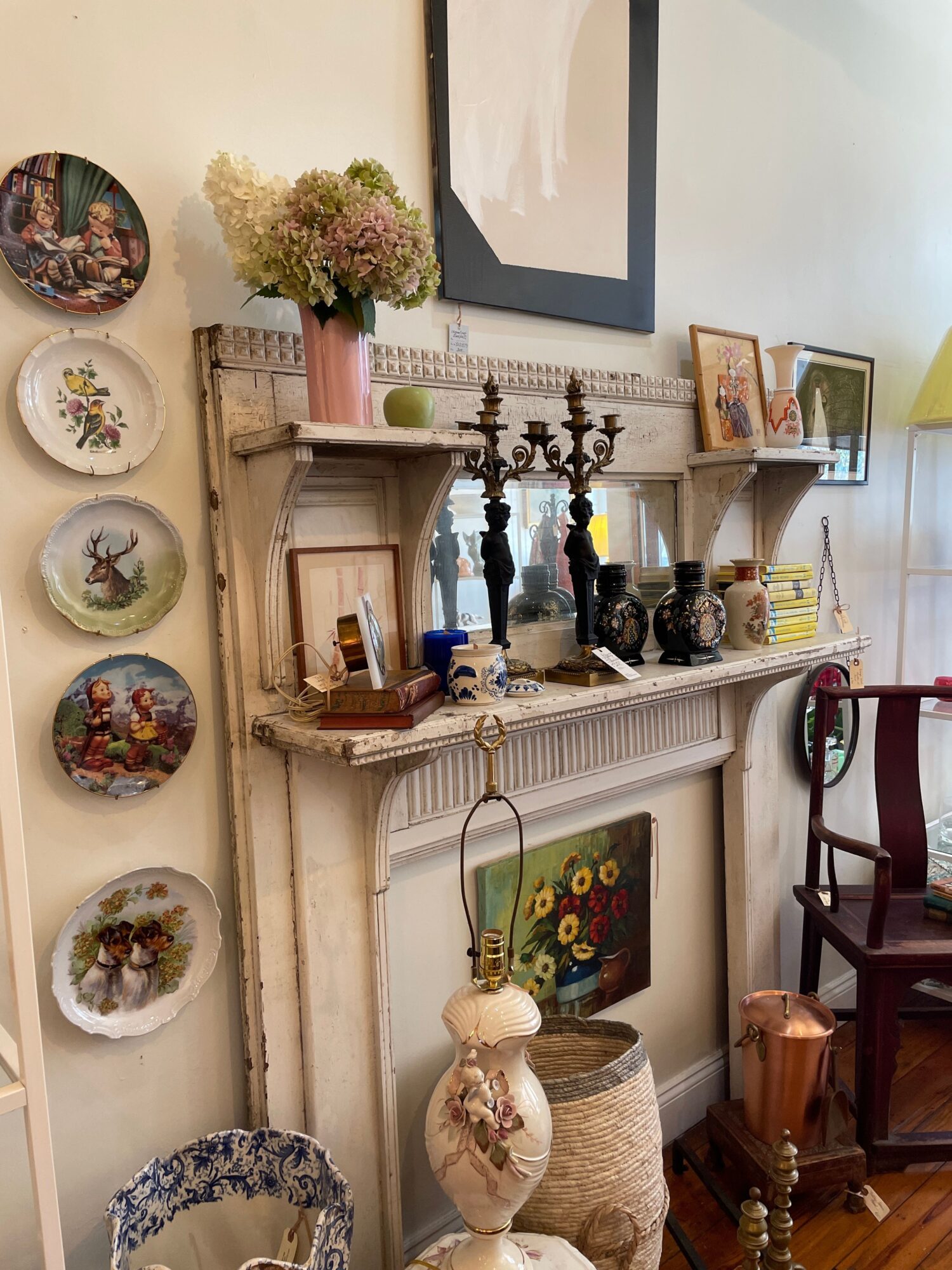 Decorative fireplace mantel with candles, vases, and framed photos, with plates and flowers below, in a cozy room.