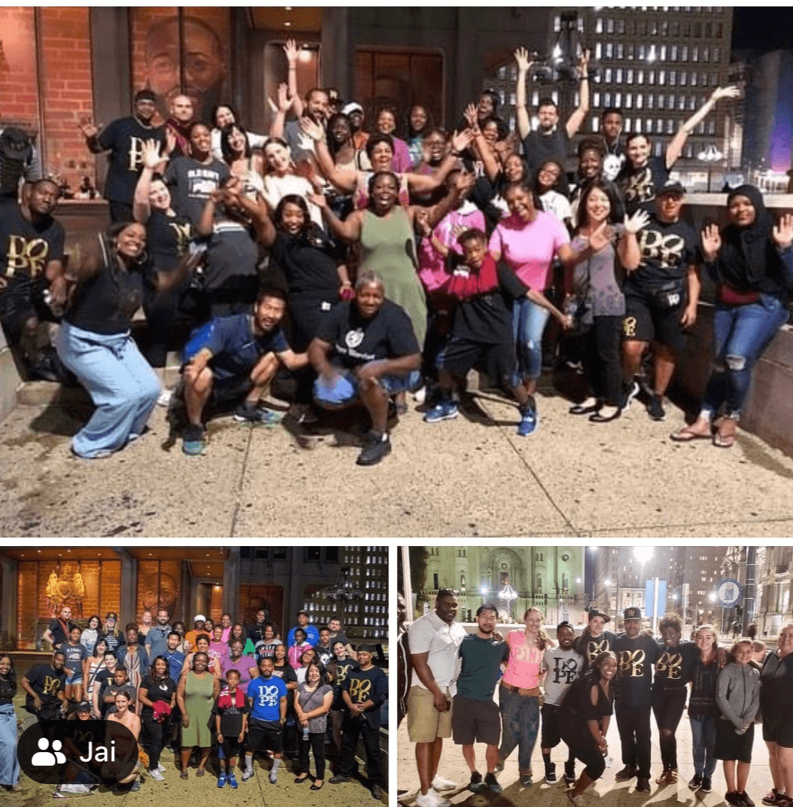 Group of people posing outdoors at night, some raising hands, in front of a brick building and city lights, diverse group, smiling.