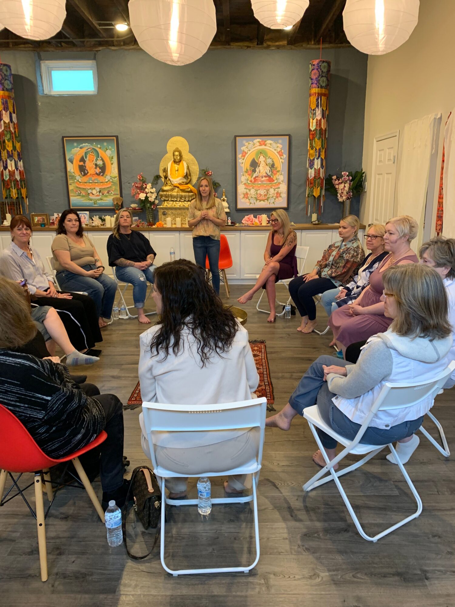 Group of people seated in a circle inside a room with Buddhist artwork and statues, listening to a speaker.