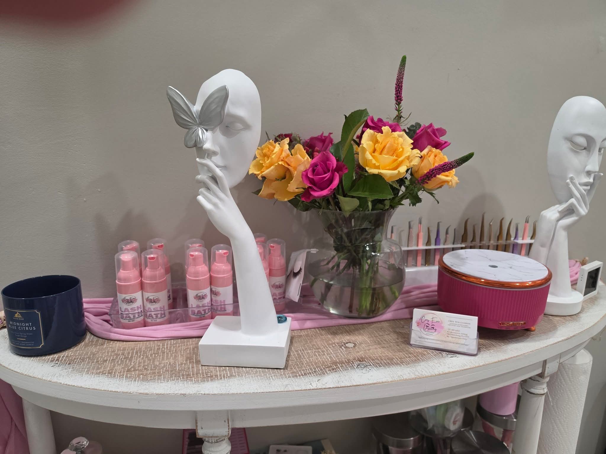 Decorative display with two mannequin heads, a bouquet of colorful roses, and various beauty products on a white table.