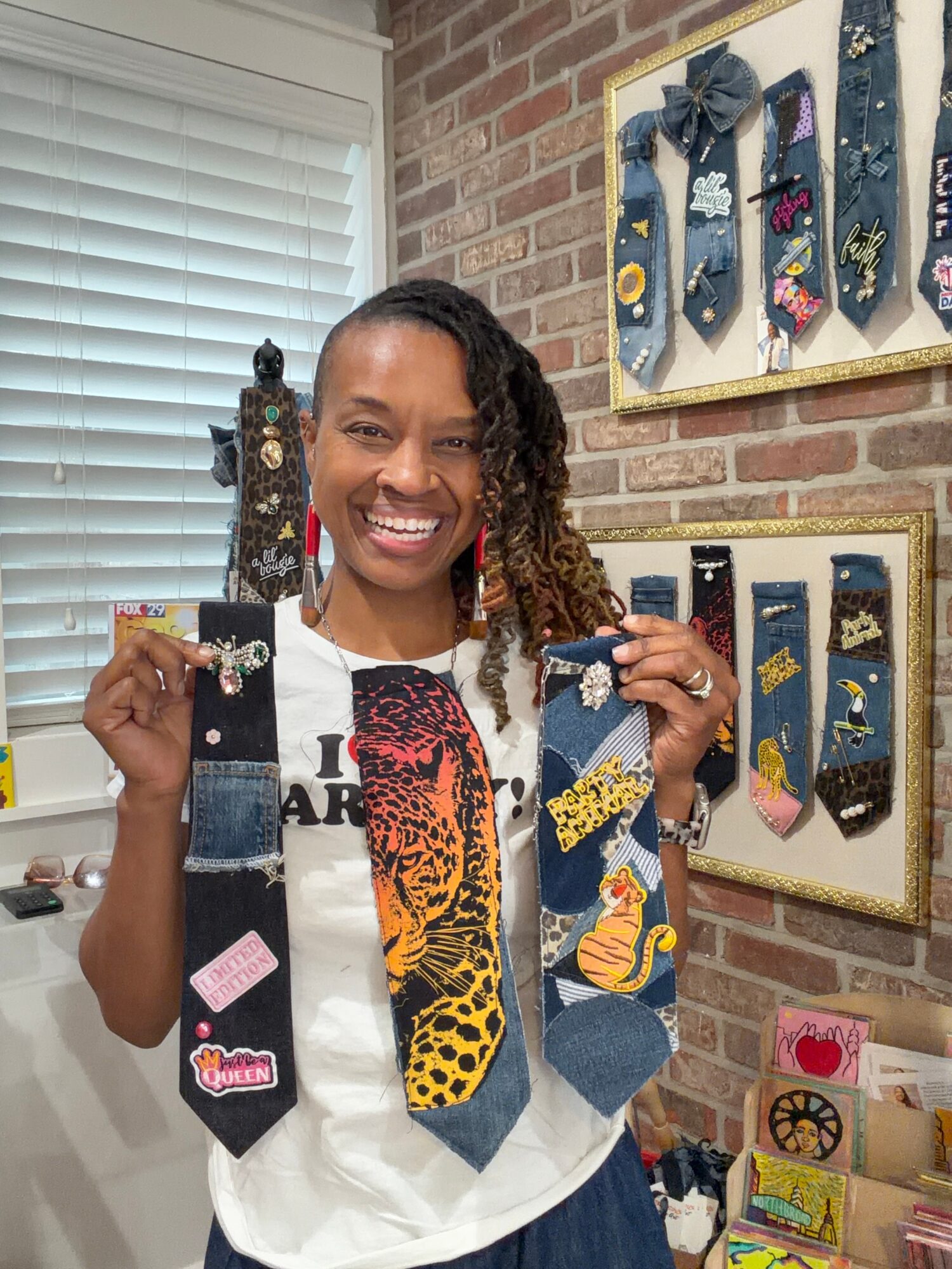 Woman smiling holding three decorated socks in front of a brick wall with framed sock art.