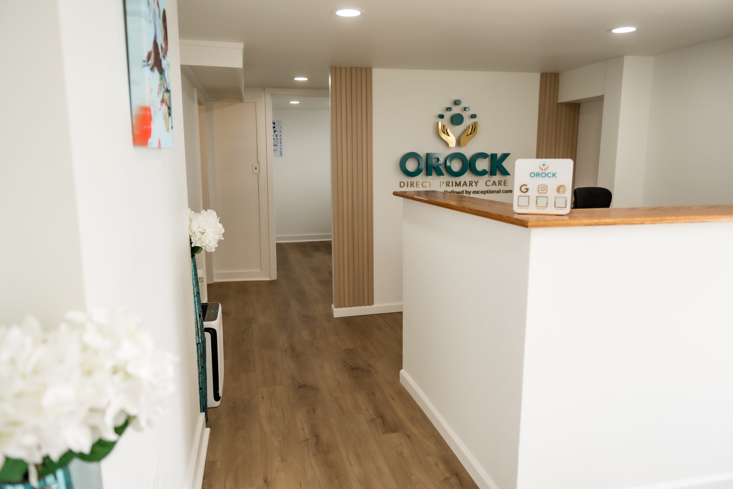 Reception area with OROCK logo on wall, white counter, and wooden accents, with a hallway in the background.