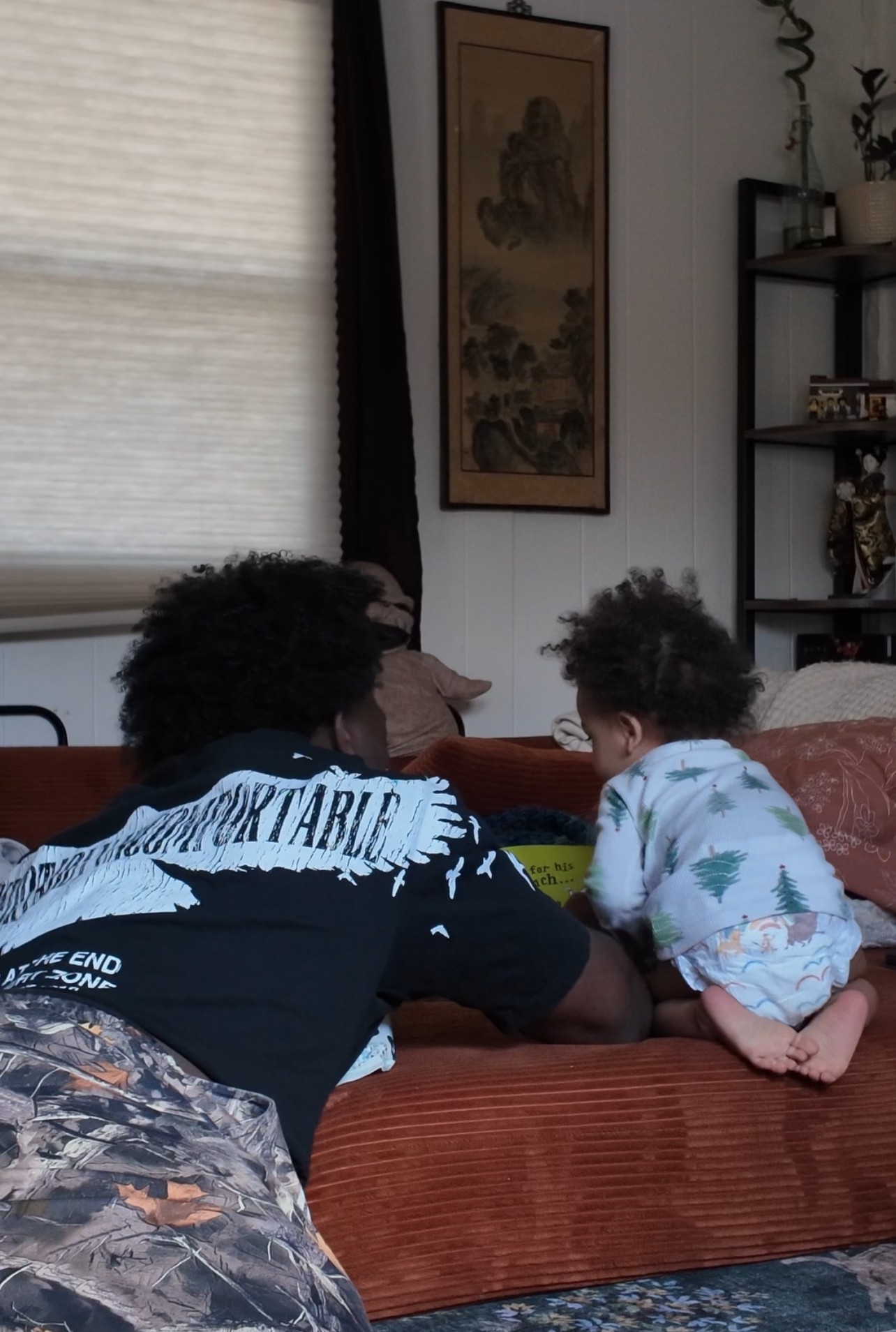 Two children with curly hair sit on a sofa facing each other in a living room, engaging in an activity.