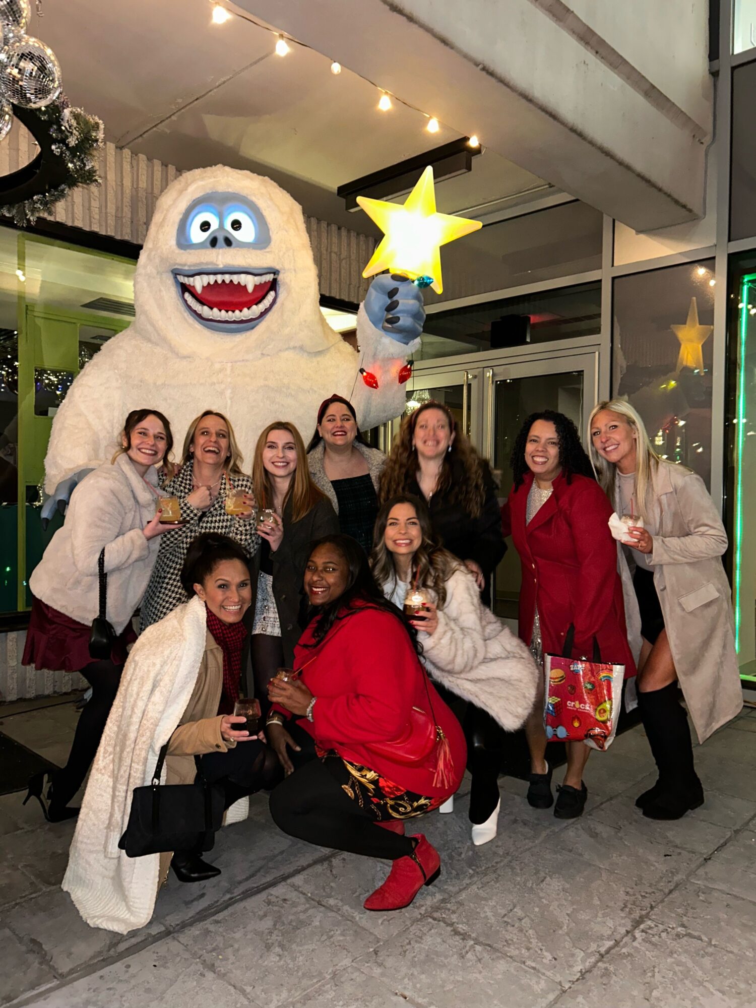 Group of people posing with a large cartoonish character costume, some holding gifts, in an indoor setting.