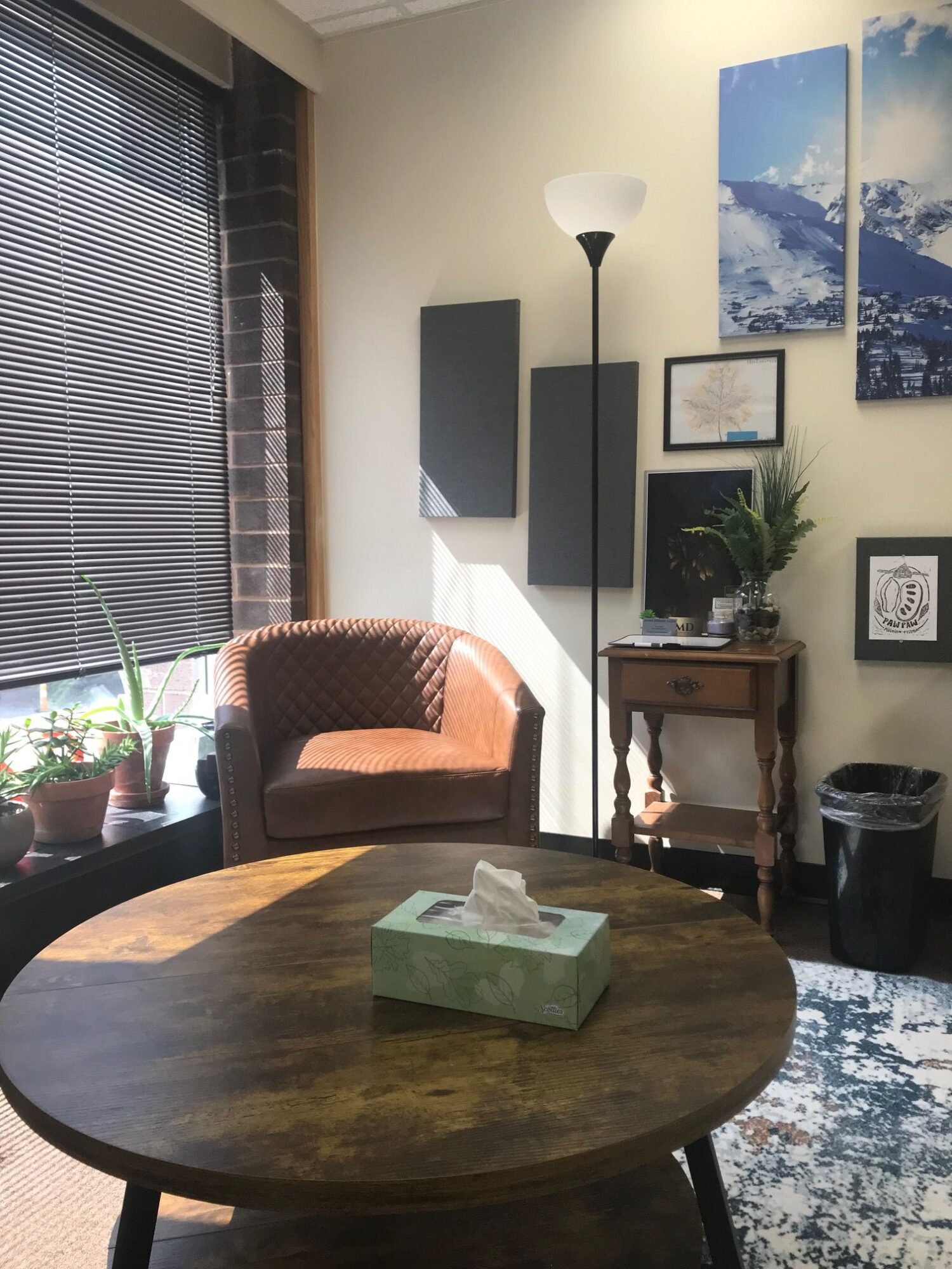 Living room with a round wooden table, a brown armchair, and wall art including a large sky photo and framed pictures.