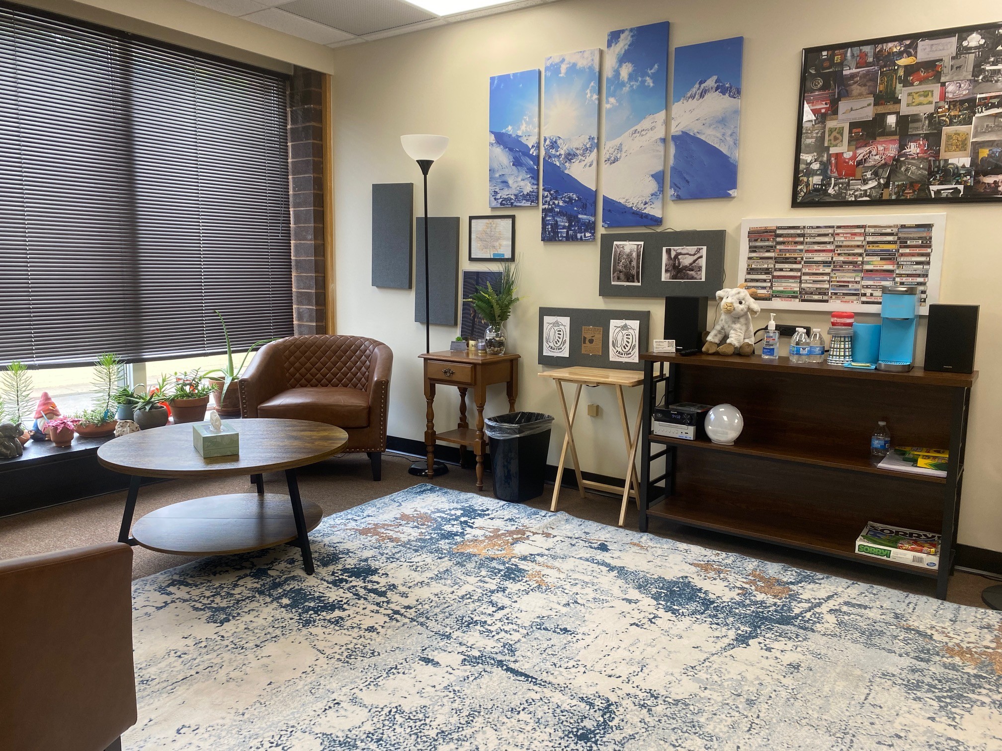 Living room with a window, brown armchair, round coffee table, and a blue and white wall art display.