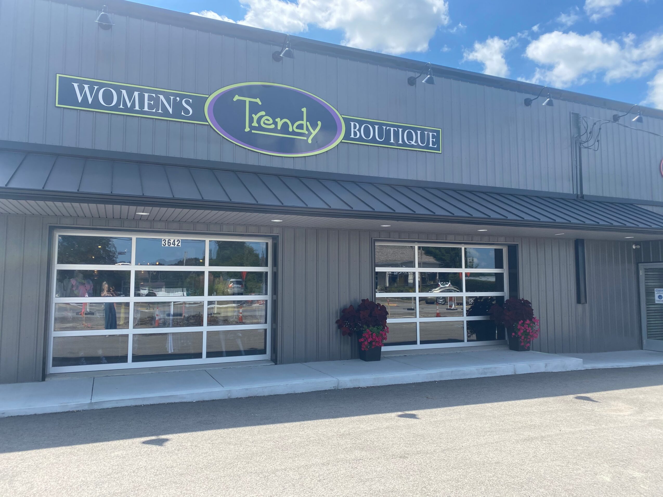 Storefront with large windows, two potted plants, and a sign reading 'Women's Trendy Boutique' against a blue sky.