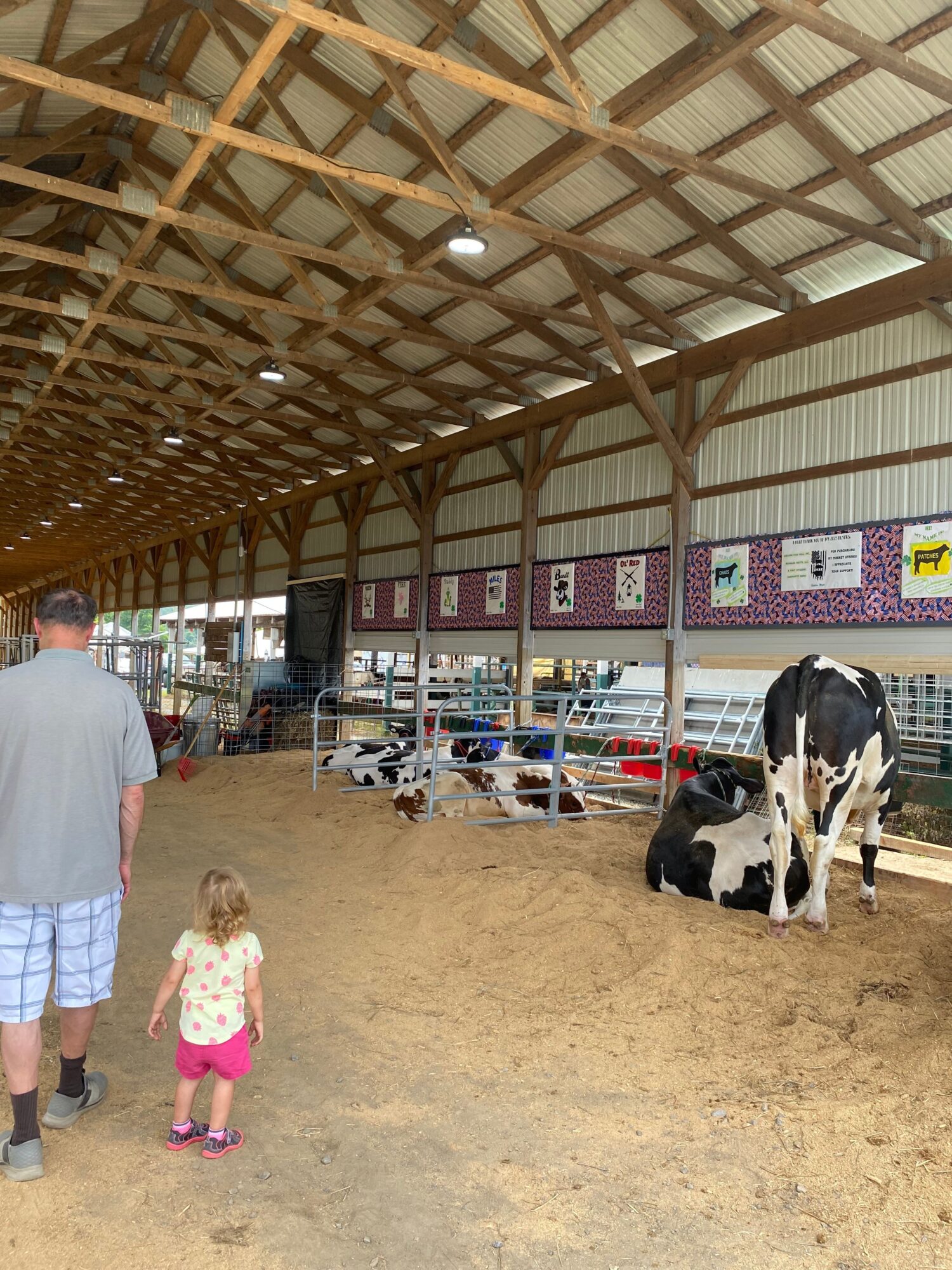 Children and a dog in an indoor space with a wooden ceiling and a dirt floor, some people in the background.