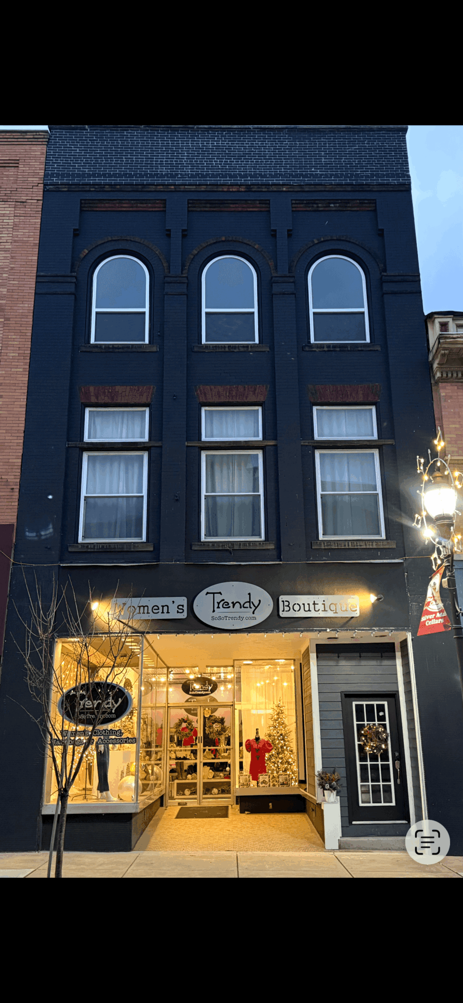 Three-story building with a storefront on the ground floor, illuminated display windows, and a sign reading 'Tandy Boutique.'