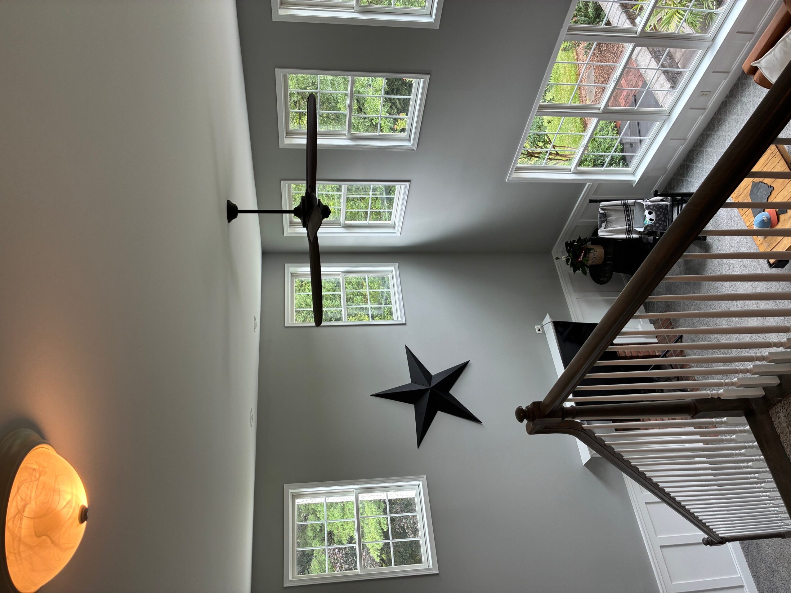 Ceiling fan with four blades, five windows with white frames, staircase railing, and a star decoration on the wall.