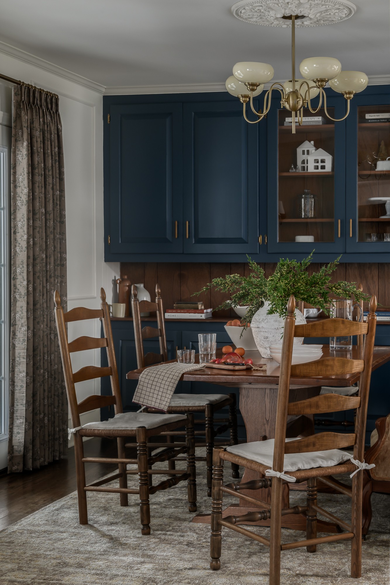 Dining area with wooden chairs around a table, blue cabinets, a chandelier, and a window with curtains.