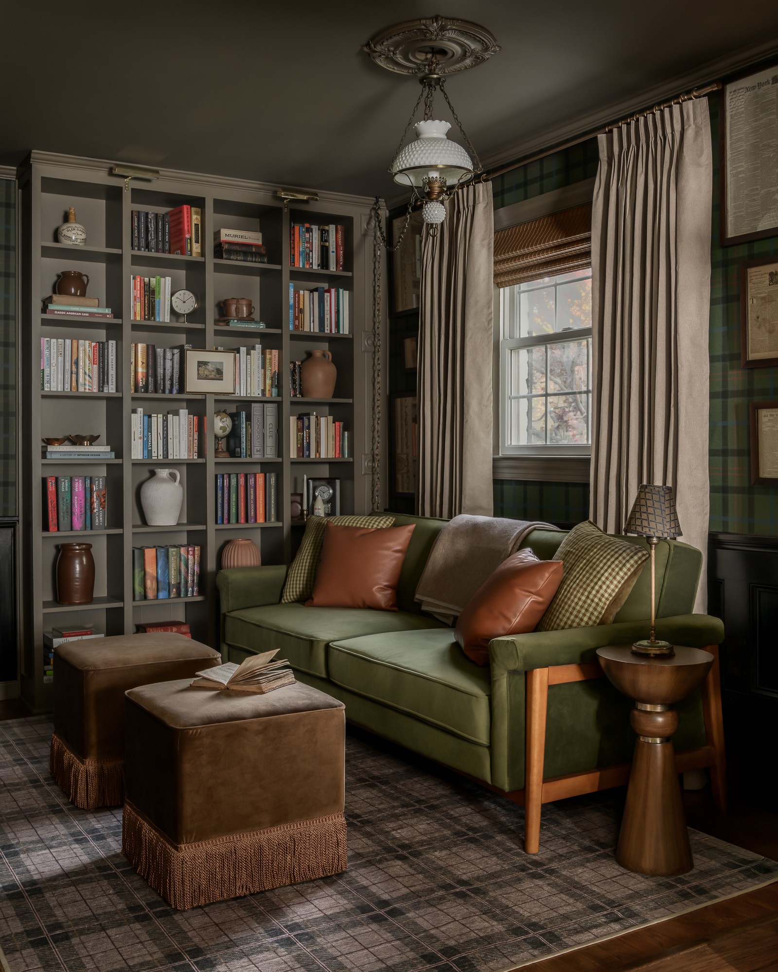 Living room with a green sofa, bookshelves, window with curtains, and a plaid rug.