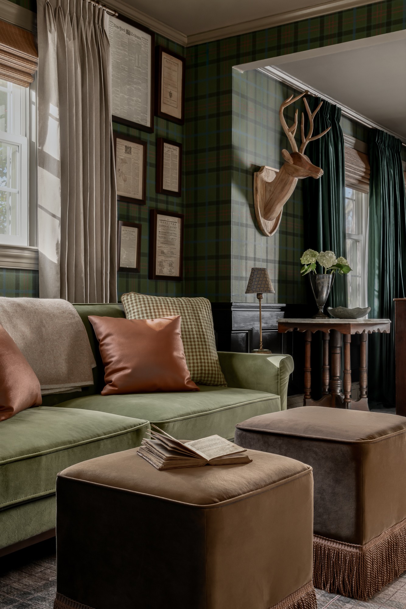 Living room with green plaid walls, a mounted deer head, framed pictures, a sofa with pillows, and a window with curtains.
