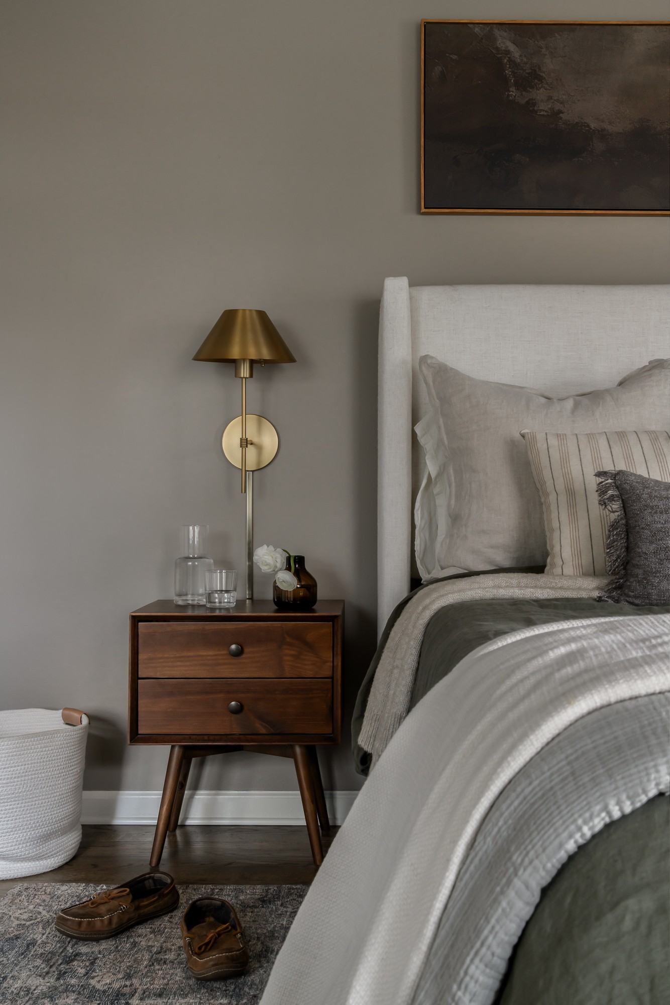 Bedroom corner with a nightstand, lamp, bed, and wall art, in neutral tones and modern decor.