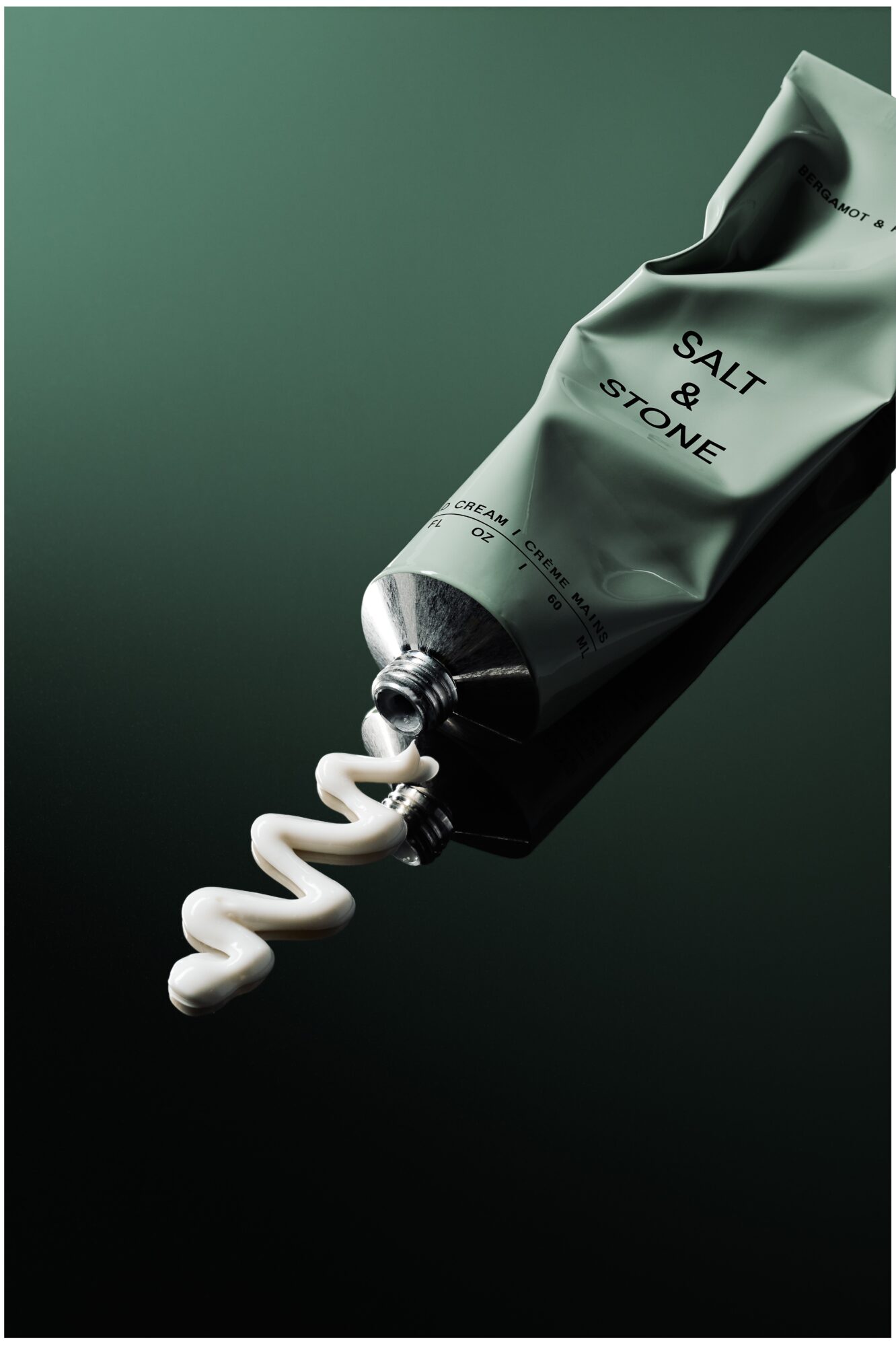 Tube labeled 'Salt & Stone' with cream squeezed out onto dark surface, shadowed background.