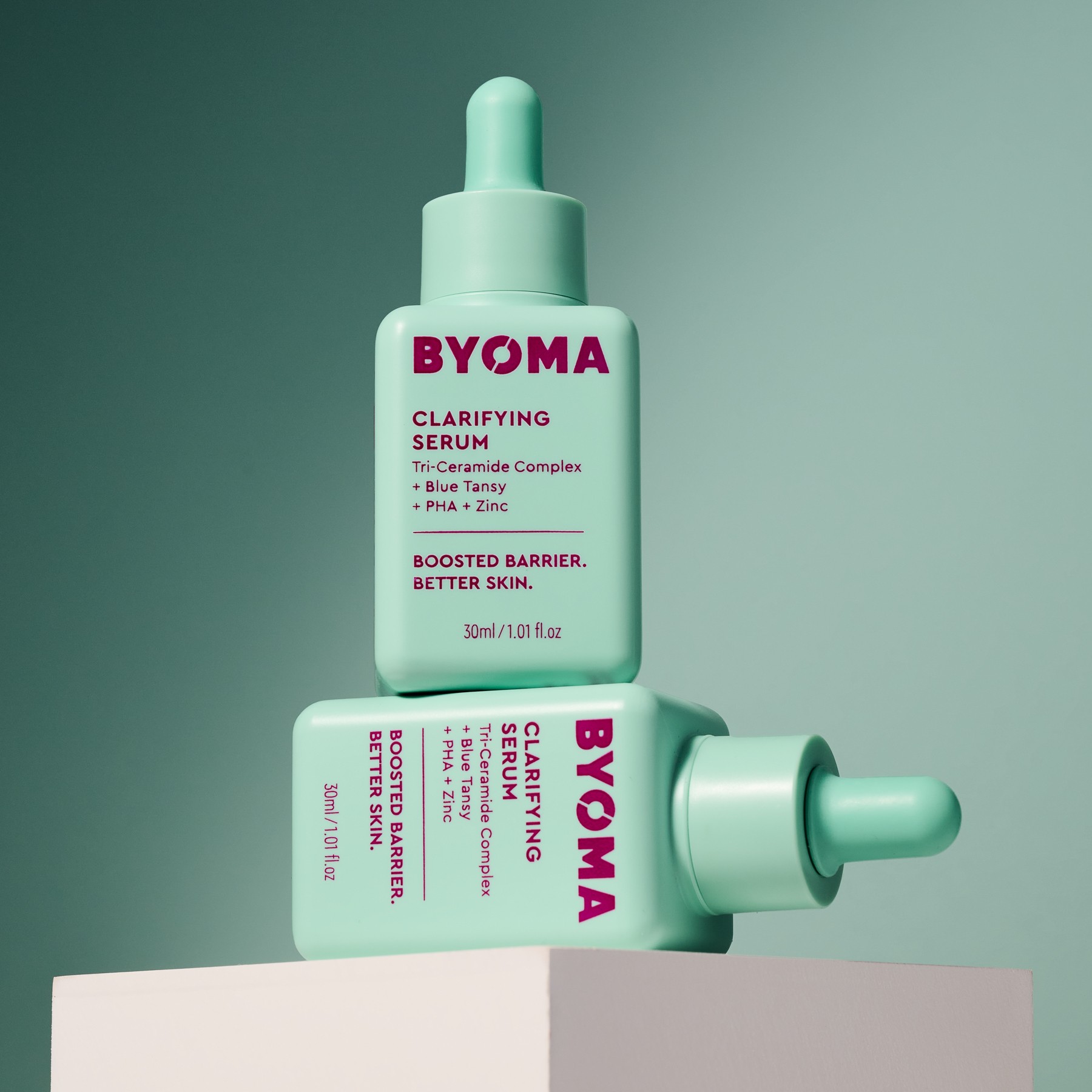 Two BYOMA skincare serum bottles, one upright and one lying on its side, on a pastel background.