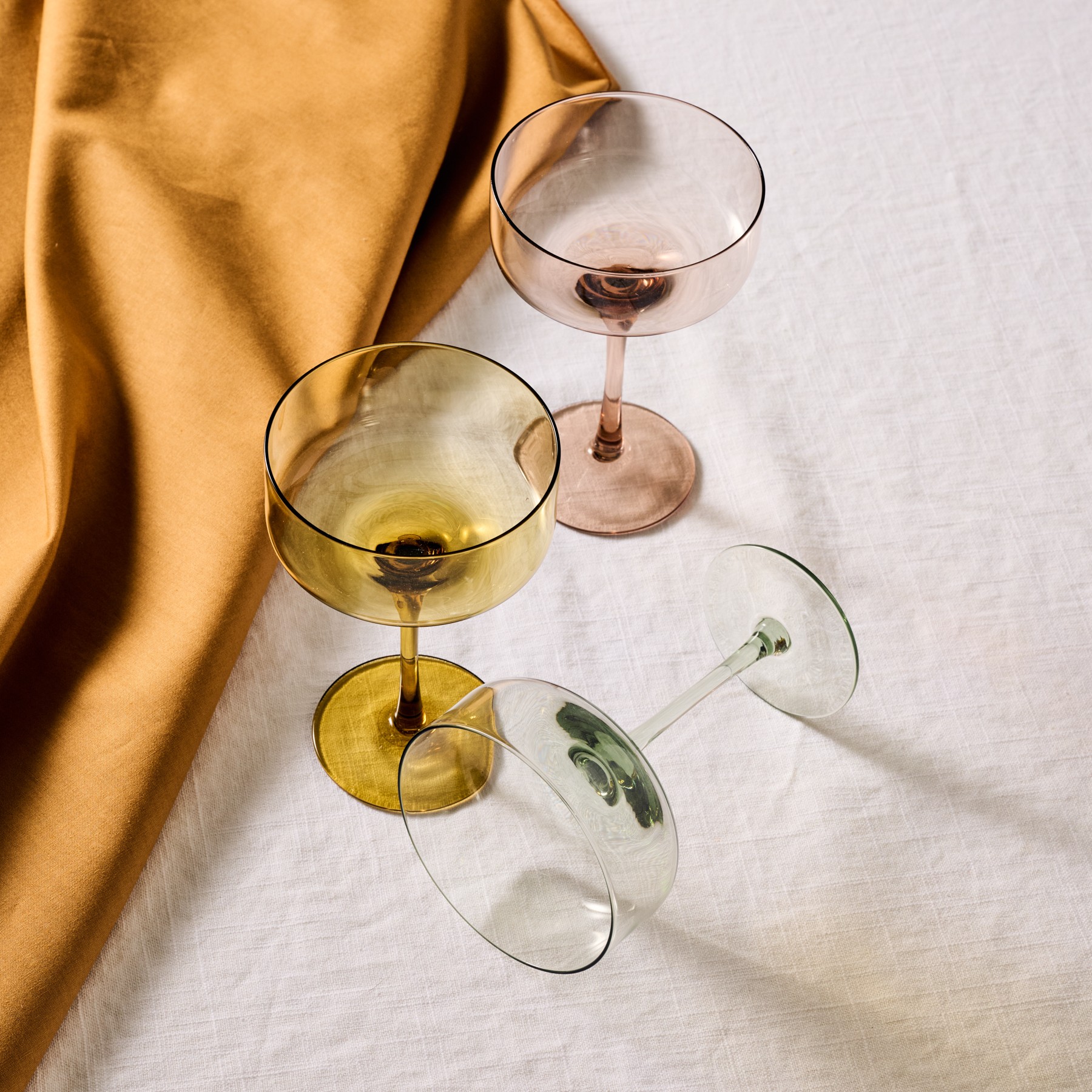Three empty wine glasses on a white surface, one with a yellow tint, one with a pink tint, and one lying on its side.