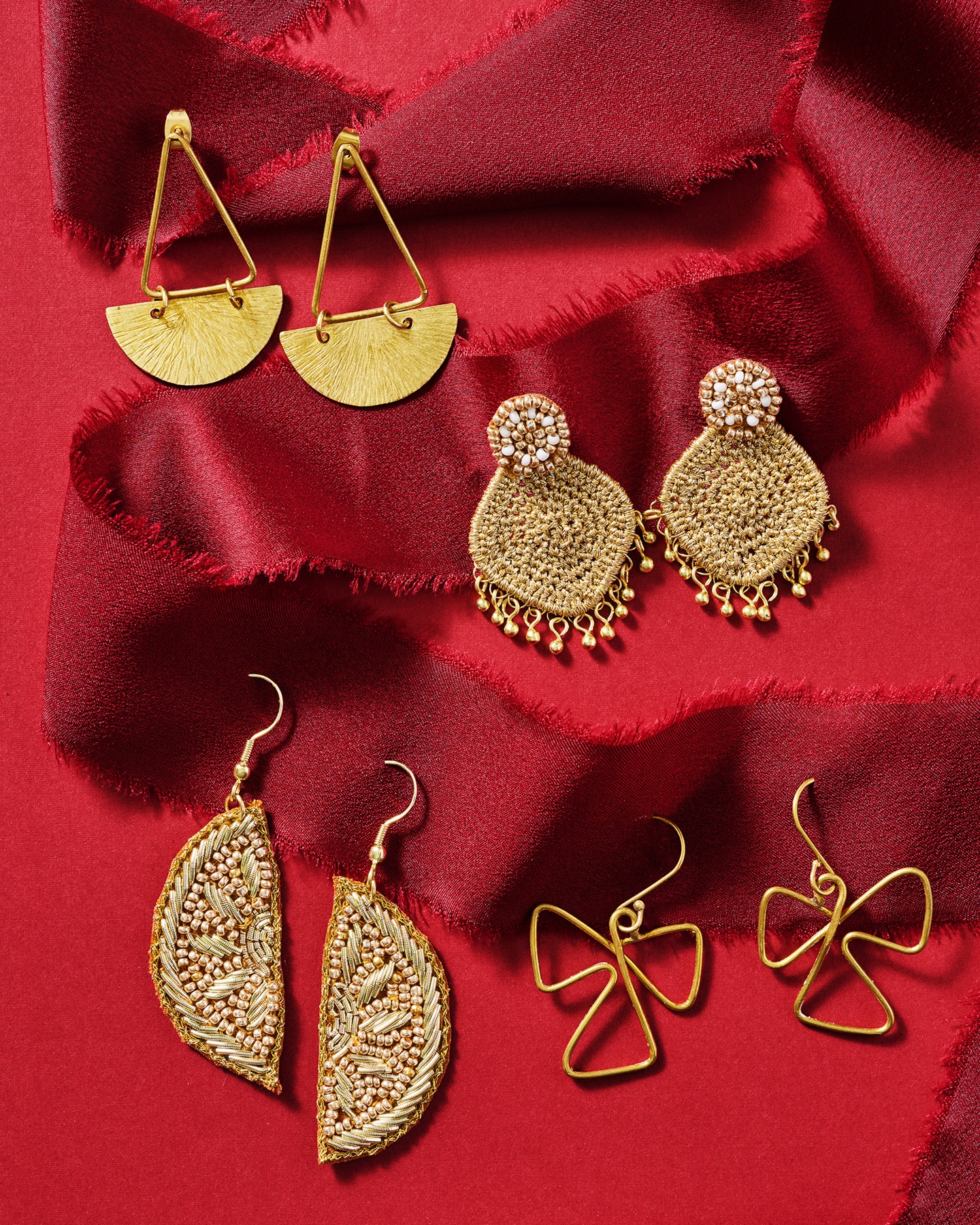 Four pairs of earrings on red satin fabric, including gold geometric, textured, floral, and bow designs.